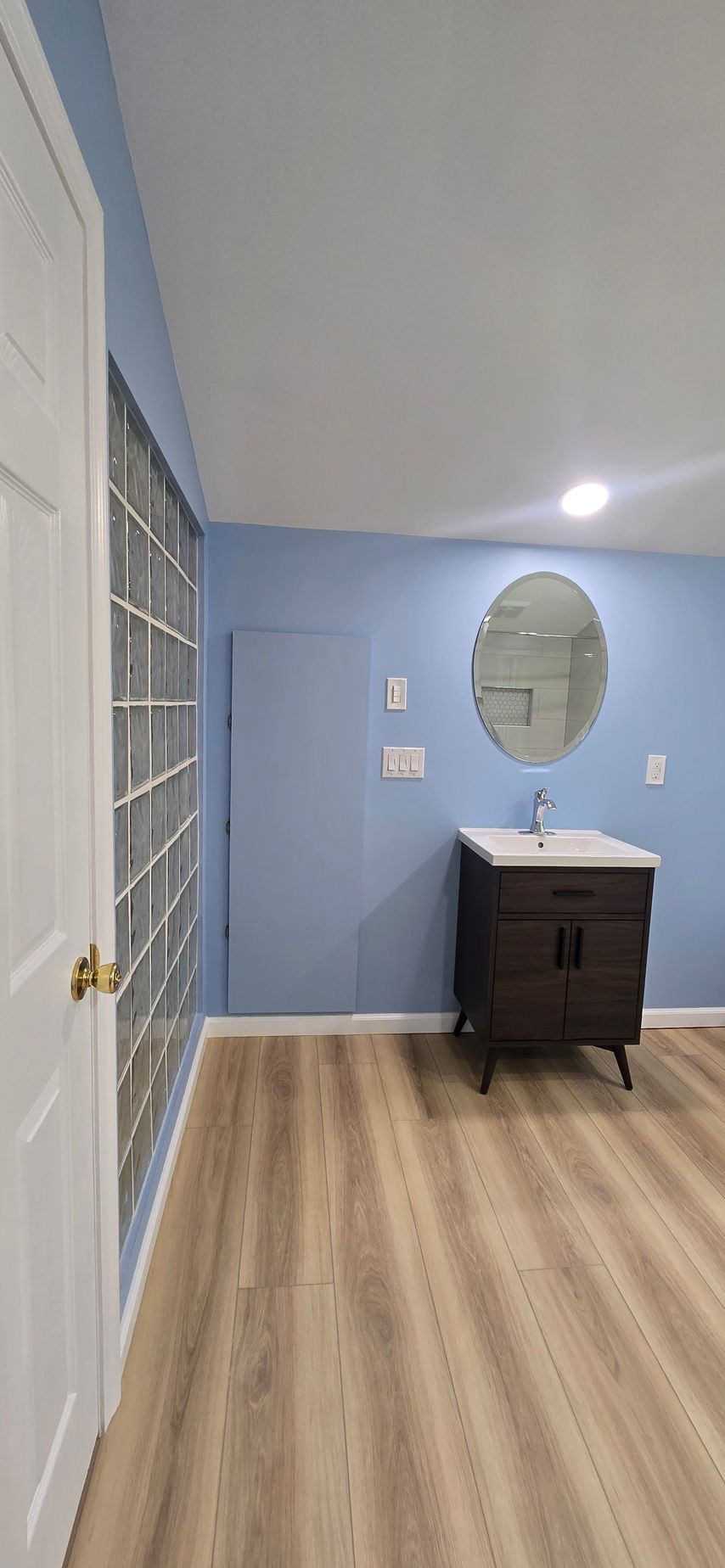Light blue hallway with wood floor, wall mirror, and a dark vanity sink under a ceiling light.