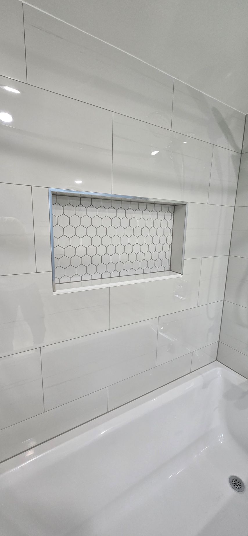 White tiled bathroom wall with recessed mirrored medicine cabinet above a bathtub.
