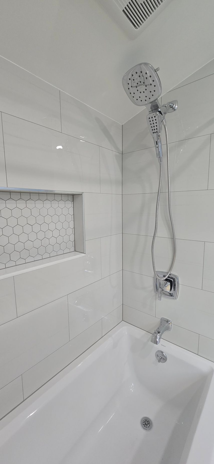 Modern white bathroom shower above a bathtub with tiled walls and a frosted window.