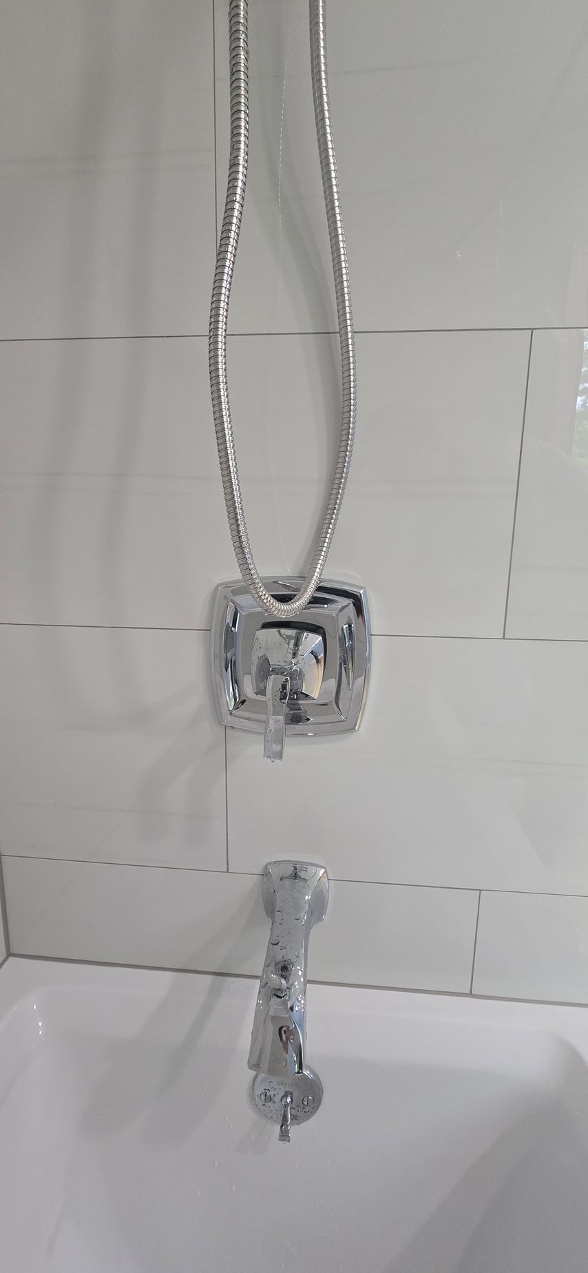 Silver necklace with a square pendant and dangling charm hanging against white tiled background