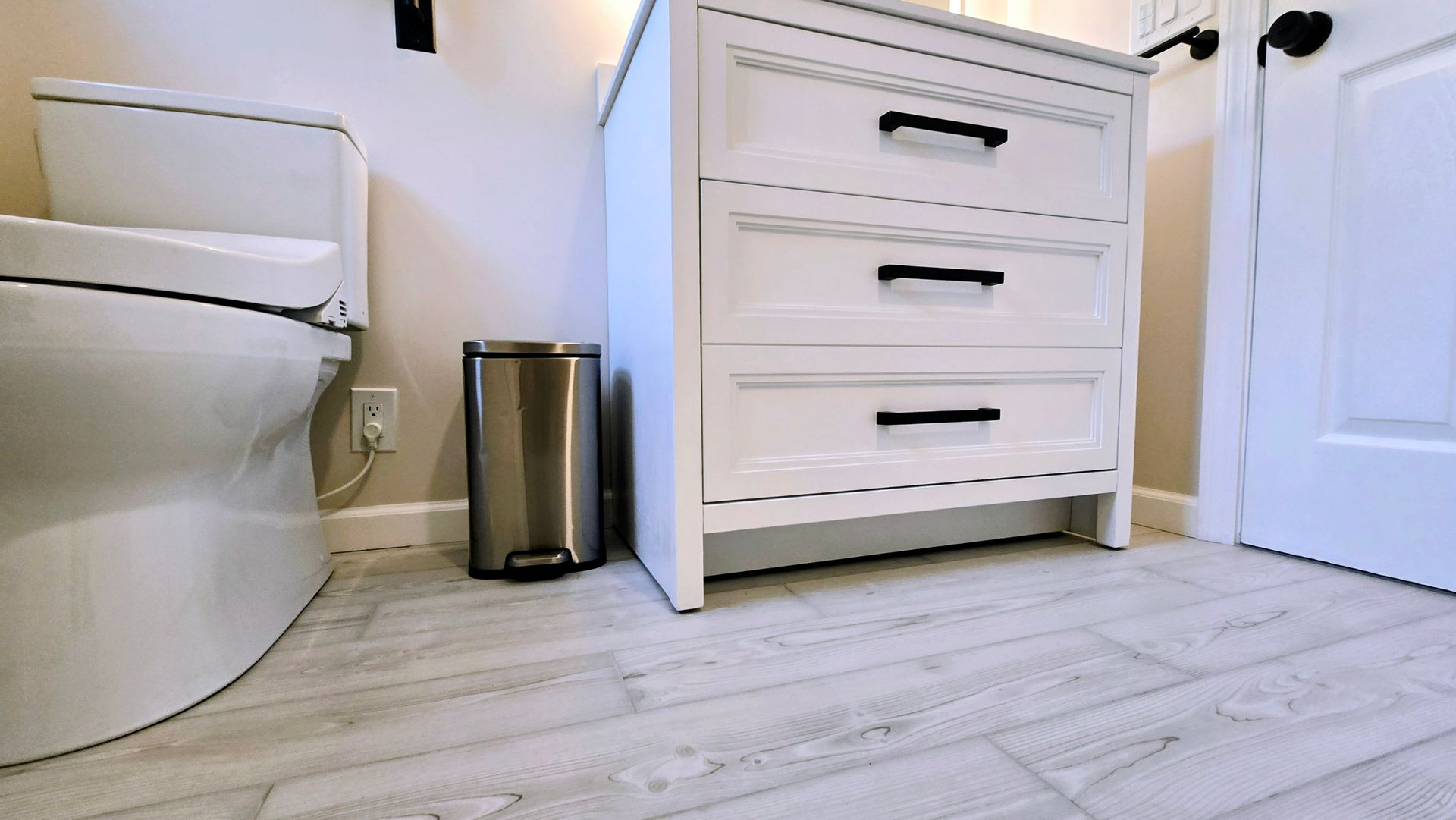 Bathroom with white toilet, trash can, and white dresser on light wood floor