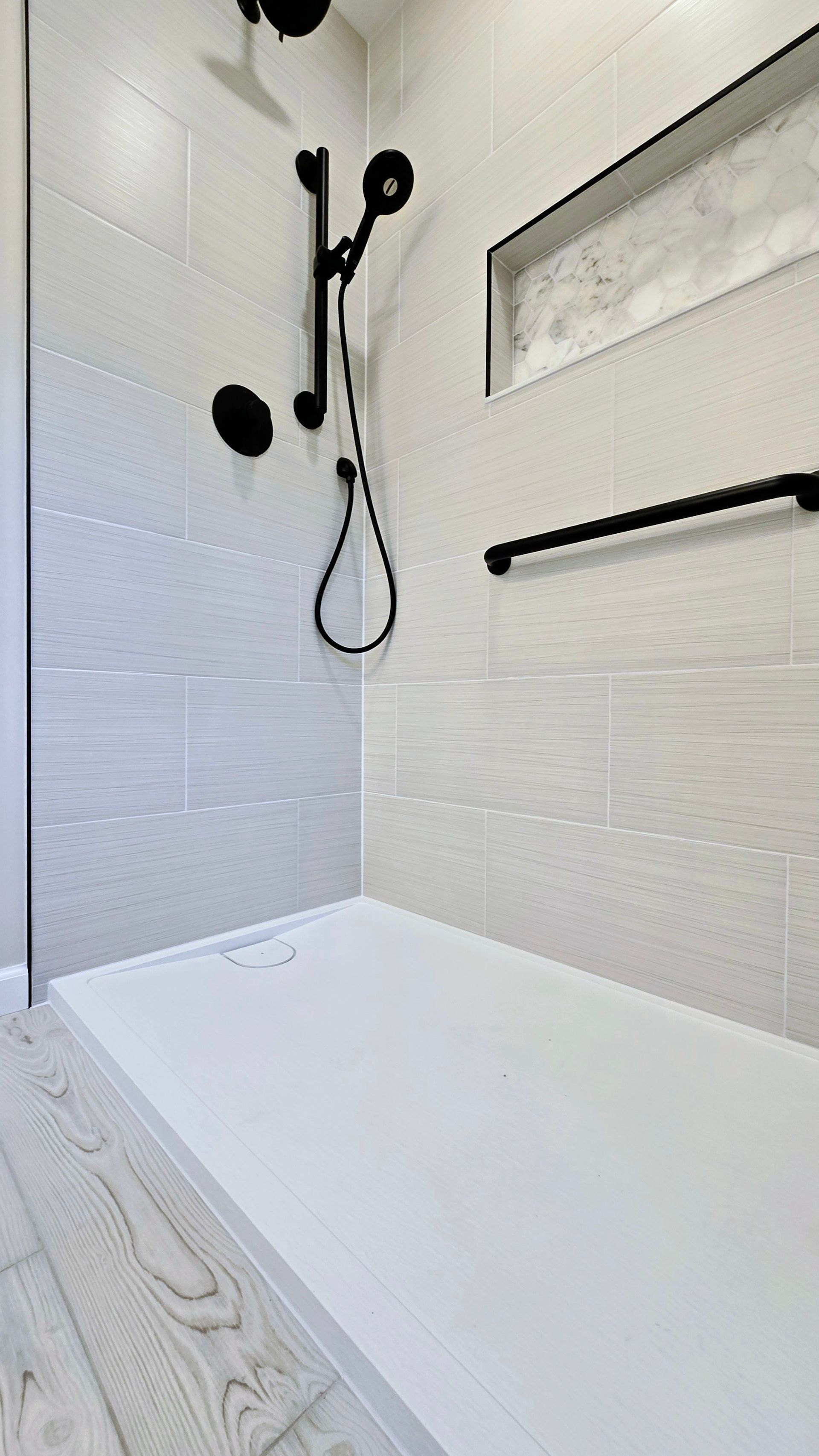 Modern white bathroom shower with tiled walls, black fixtures, and a wall mirror