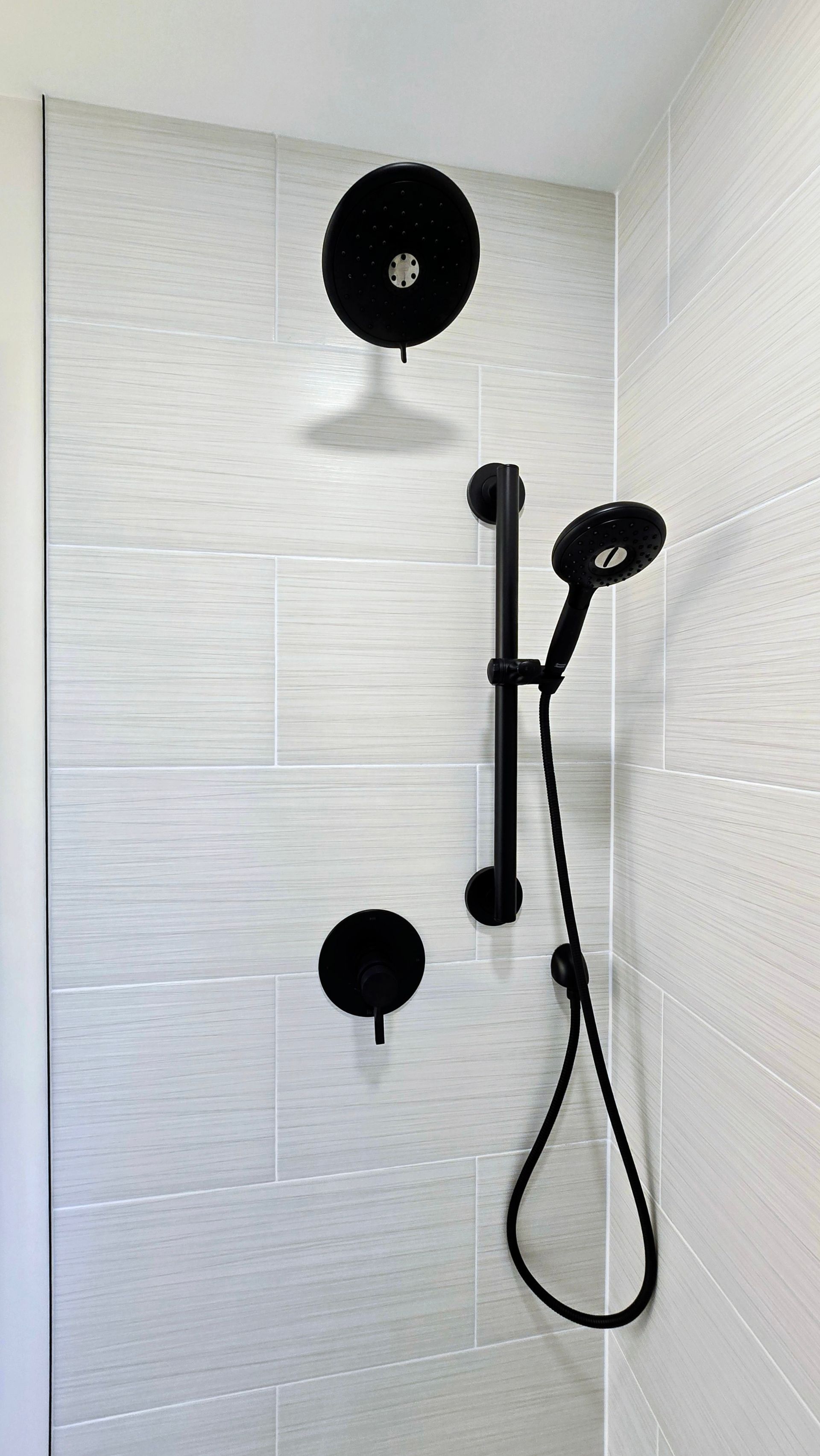 White tiled shower with black shower fixtures and handheld showerhead.