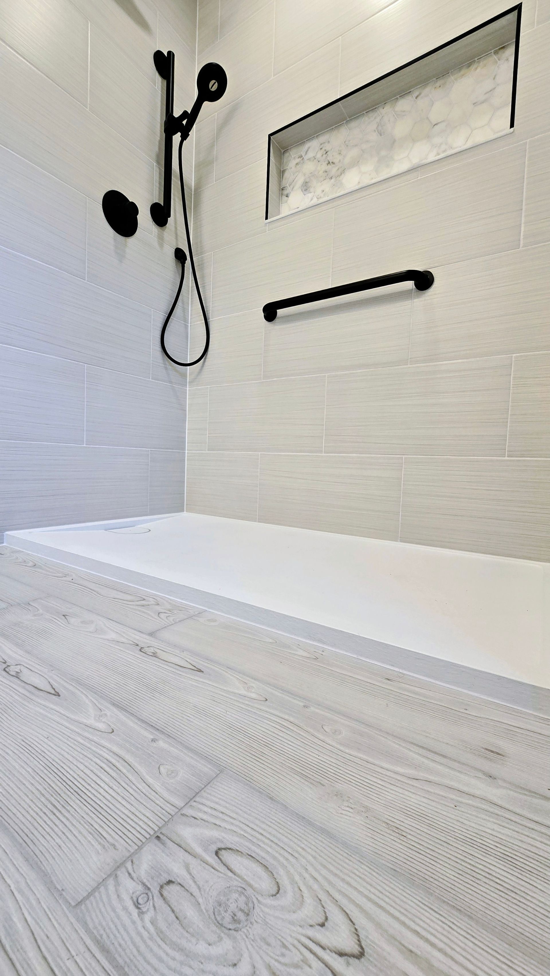 Modern white shower remodel in Manchester, CT with built-in shelf, grab bar, and black handheld showerhead on tiled wall