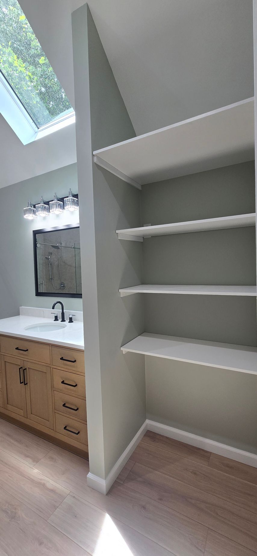 Built-in white shelving nook beside a bathroom vanity under a slanted ceiling.