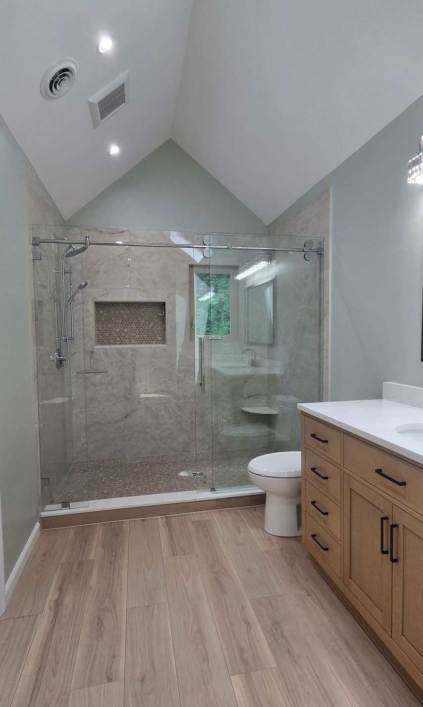Modern bathroom with glass shower, toilet, and wood vanity under a sloped ceiling