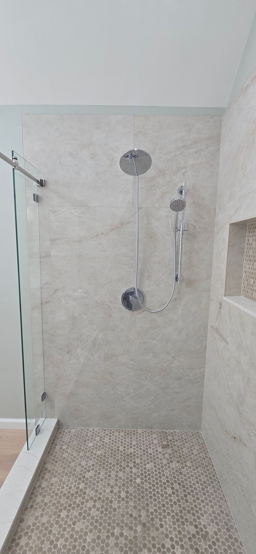 Walk-in shower with glass door, tiled walls, pebble floor, and a wall-mounted showerhead.