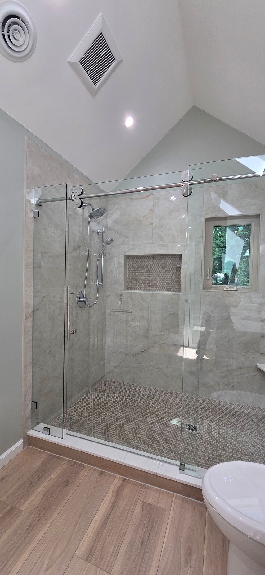 Bright modern bathroom with glass shower enclosure, marble tile, and light wood floor
