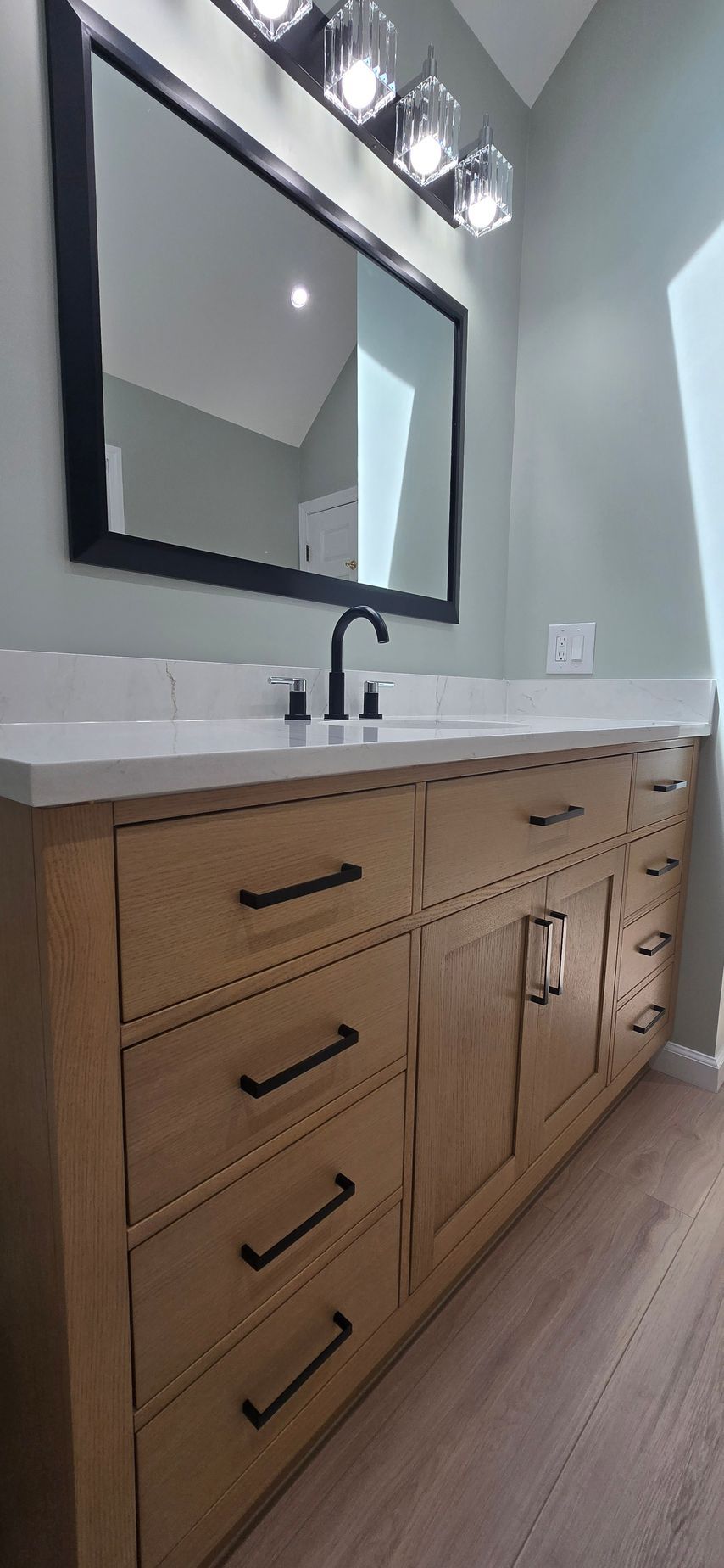 Modern bathroom vanity with wood cabinets, black faucet, large mirror, and vanity lights