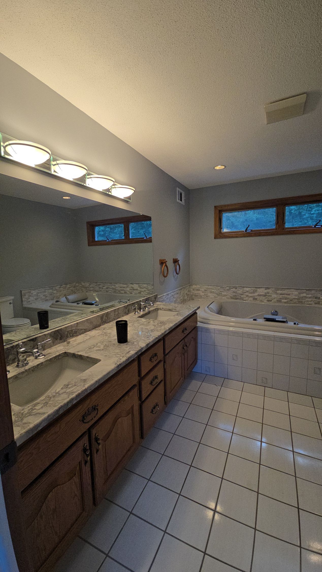 The before bathroom in Rocky Hill, CTwith double vanity, large mirror, tiled floor, and white bathtub by small windows.