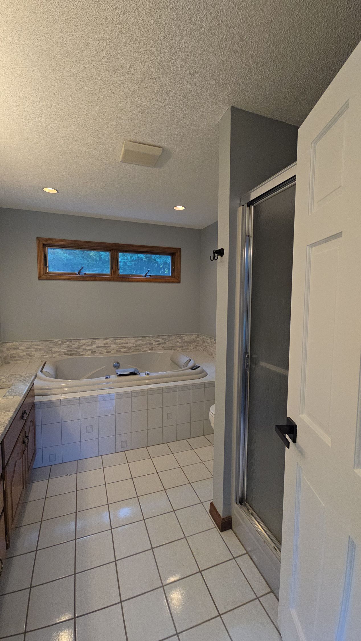 The before bathroom in Rocky Hill, CT with small tiled bathroom with a bathtub, white cabinet, and narrow window under a sloped ceiling.
