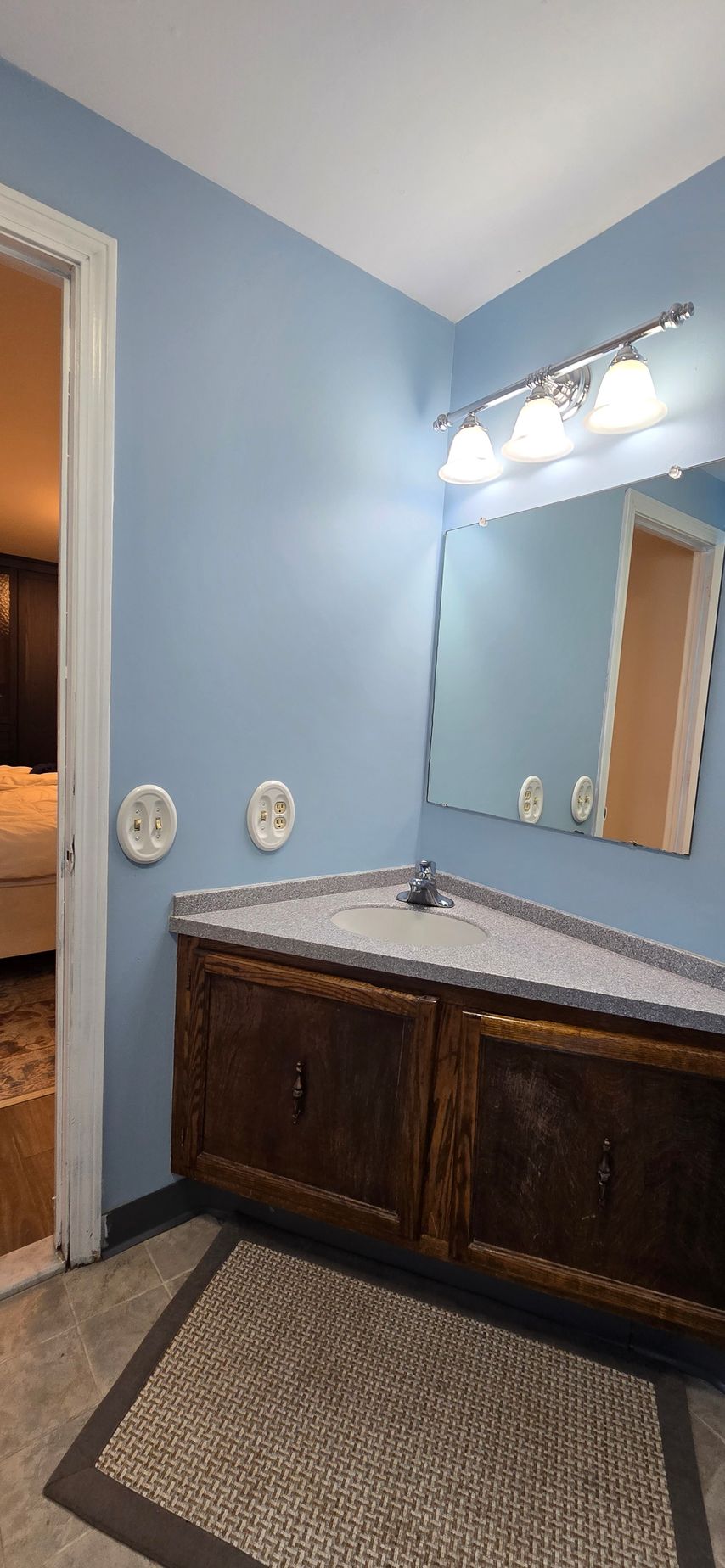 Bathroom vanity with blue walls, double sinks, and a large mirror above a dark wood cabinet. By First Choice Bathroom Remodeling done in Glastonbury CT.