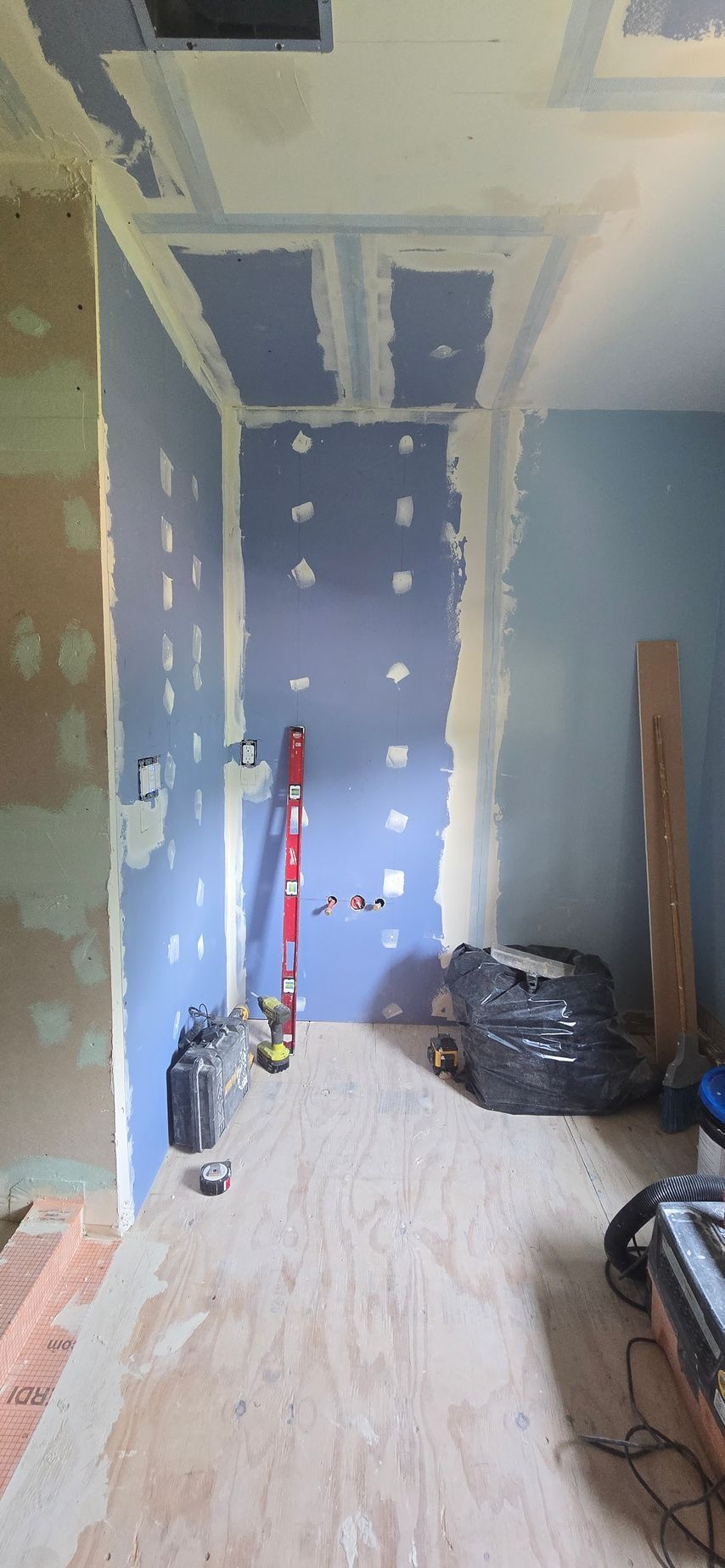 Narrow hallway under renovation with blue drywall, white ceiling patches, and tools on the floor. By First Choice Bathroom Remodeling done in Glastonbury CT.