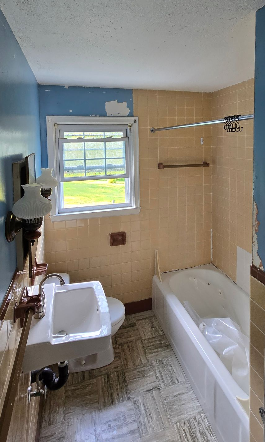 Small bathroom in Manchester, CT with beige tile, white tub, toilet, window, and a shower curtain rod.