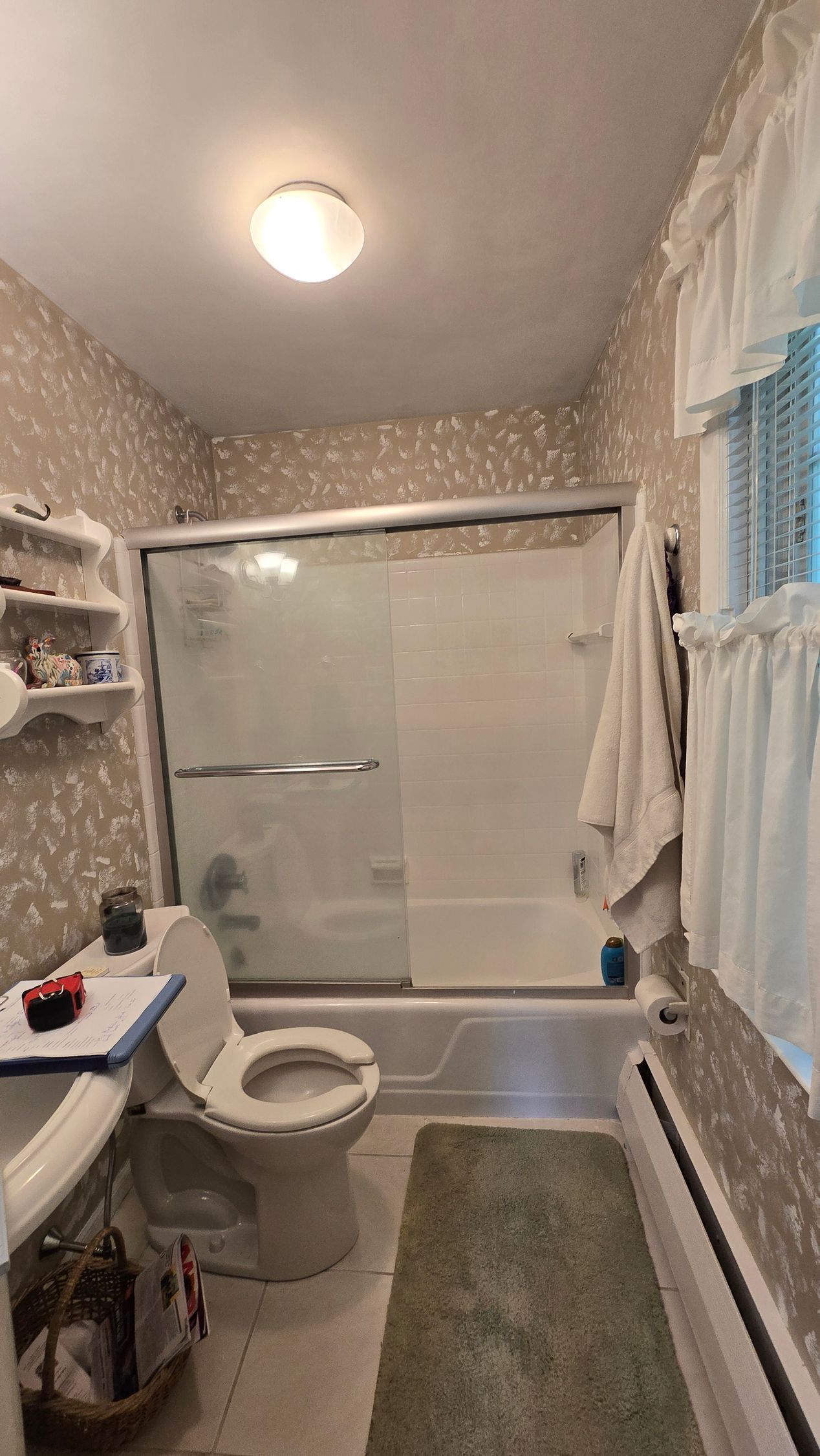Small bathroom with a toilet, bathtub shower, sink, shelves, and a green rug. By First Choice Bathroom Remodeling done in Avon, CT.