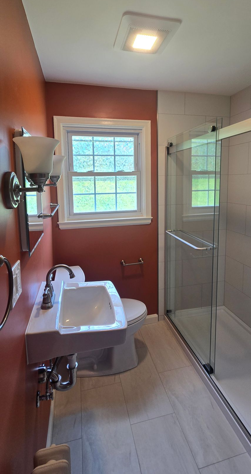 Bathroom with white vanity sink, window, shower stall, and red accent wall