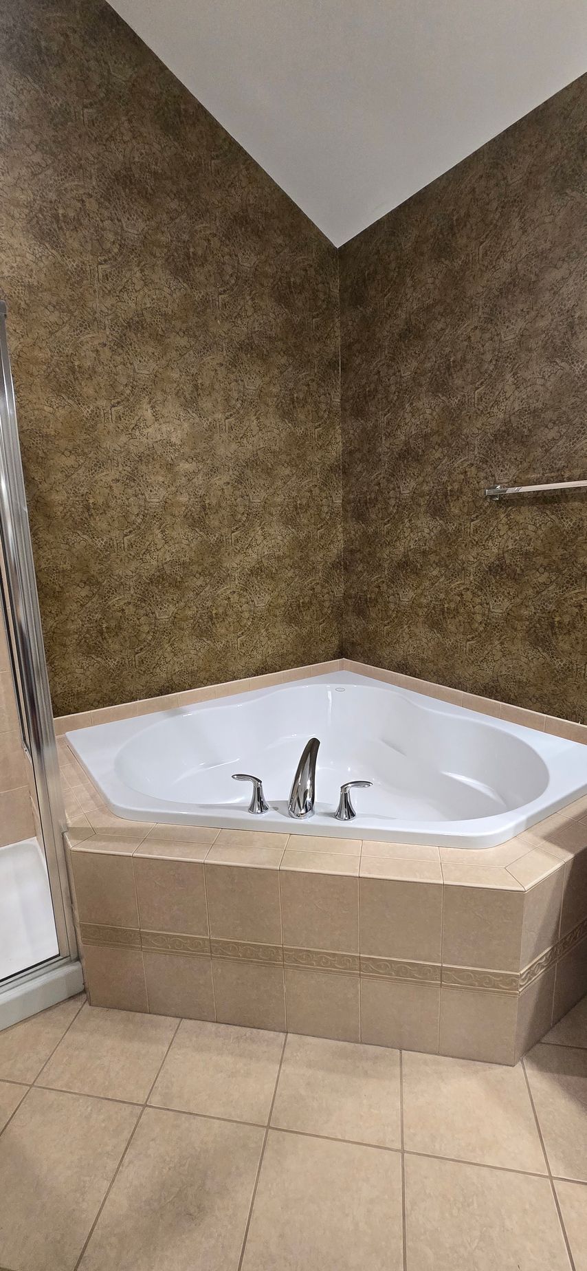 Corner bathroom with a white corner soaking tub in Prospect, CT, beige tile floor, and brown textured walls.