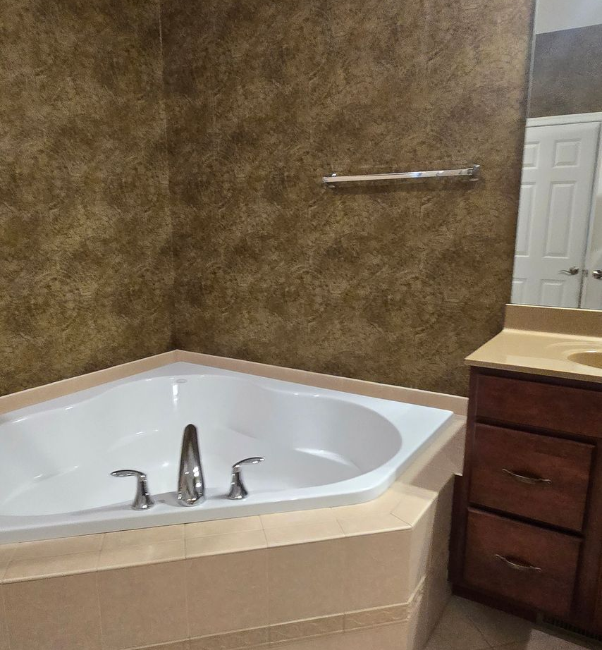 Corner bathroom with a jetted tub, brown textured walls, and a dark wood vanity.