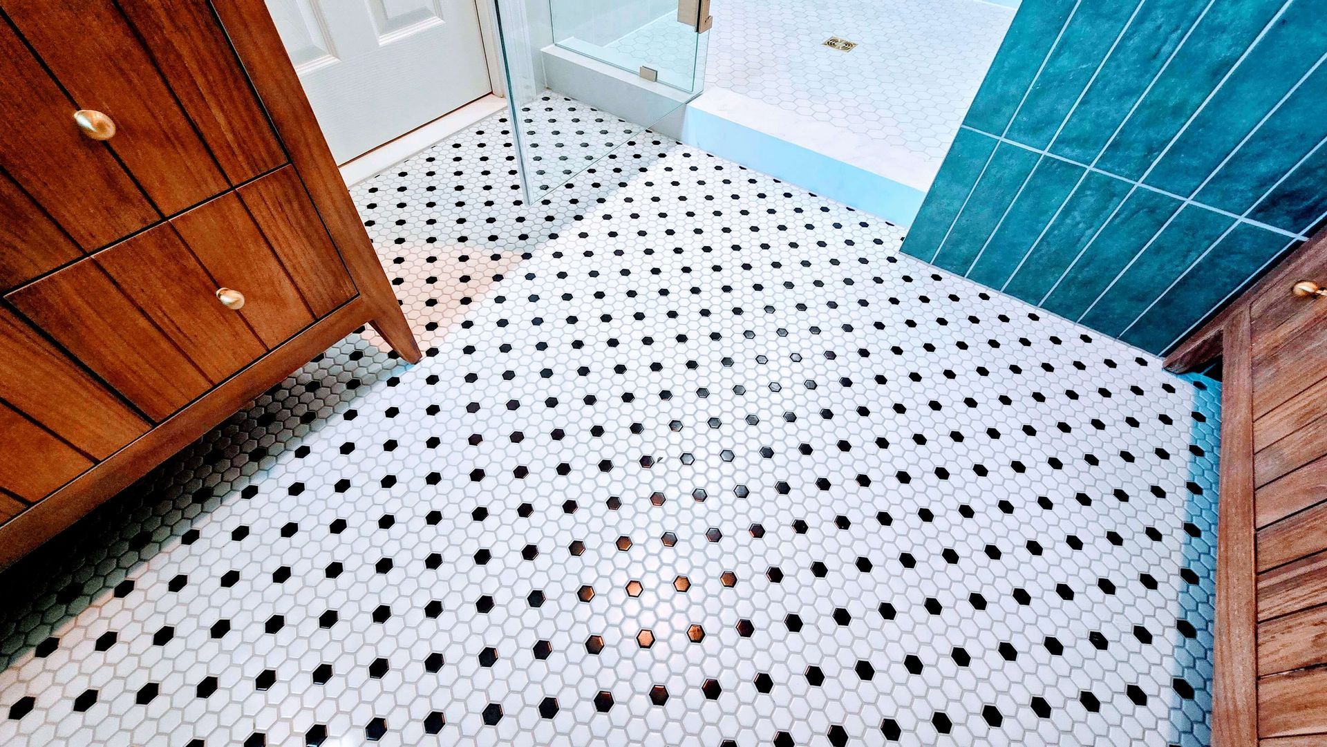 Bathroom with white hex tile floor in Glastonbury, CT, teal shower tiles, and a wooden cabinet on the left.