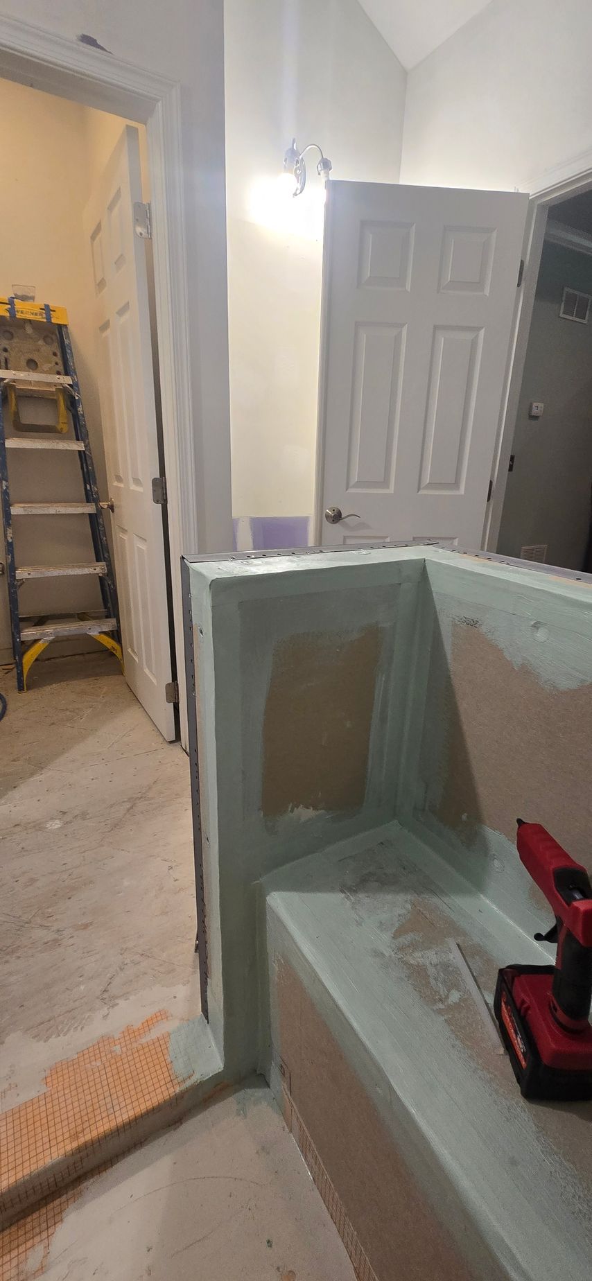 Partially finished room with a ladder, open door, and a red drill on a half-built wall. By First Choice Bathroom Remodeling done in Prospect, CT.