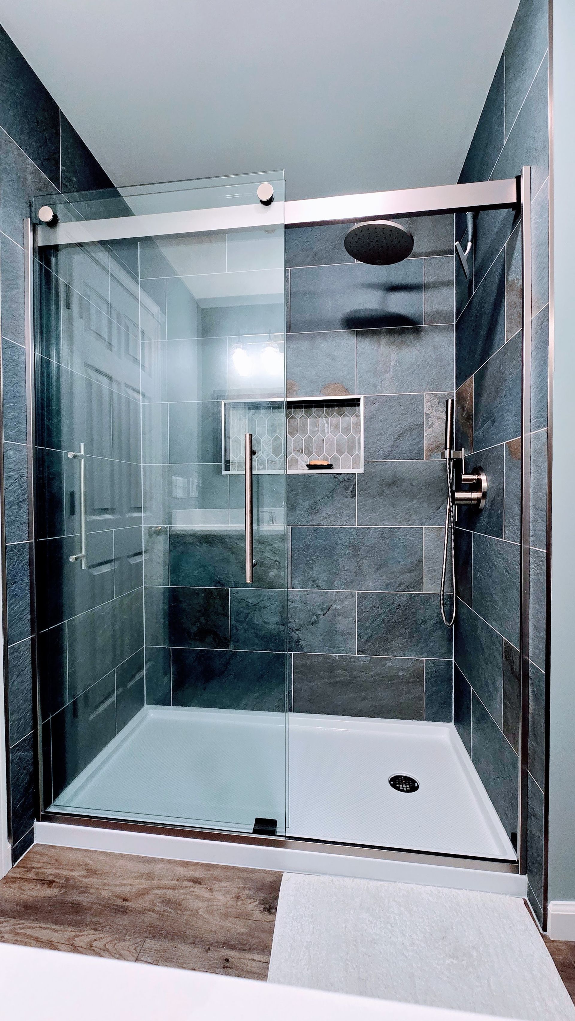 Modern walk-in shower in Plainville, CT with glass shower enclosure with gray tile walls, rainfall showerhead, and open door.