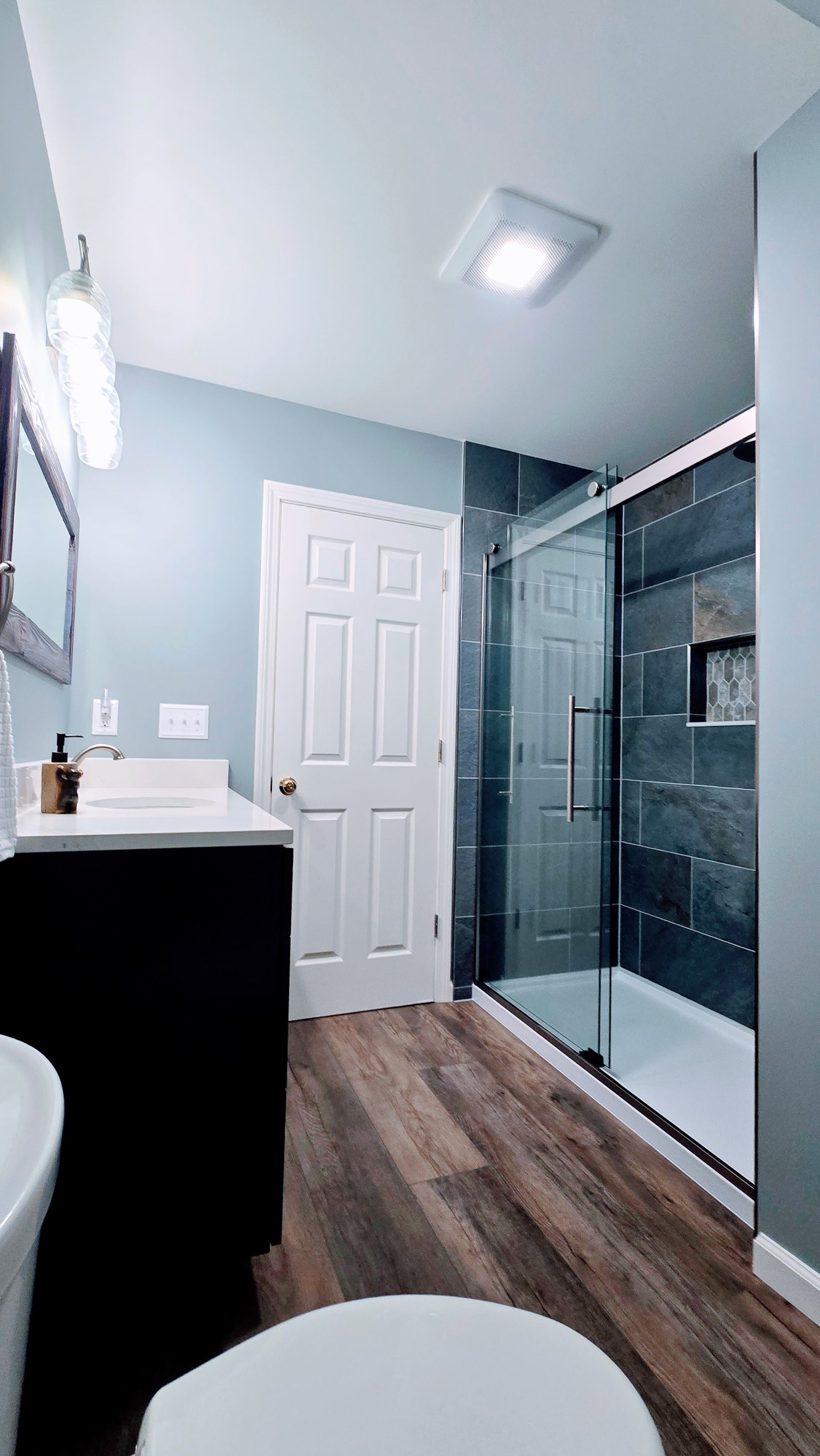 Modern bathroom with white vanity, glass shower, and wood-look flooring. By First Choice Bathroom Remodeling done in Plainville CT.