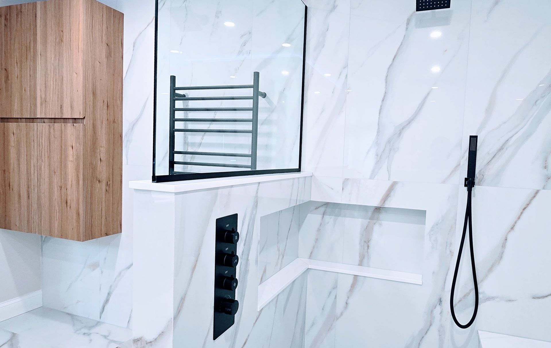 Modern bathroom in Southington, CT with white marble walls, wooden cabinet, mirror, towel rack, and black shower fixture
