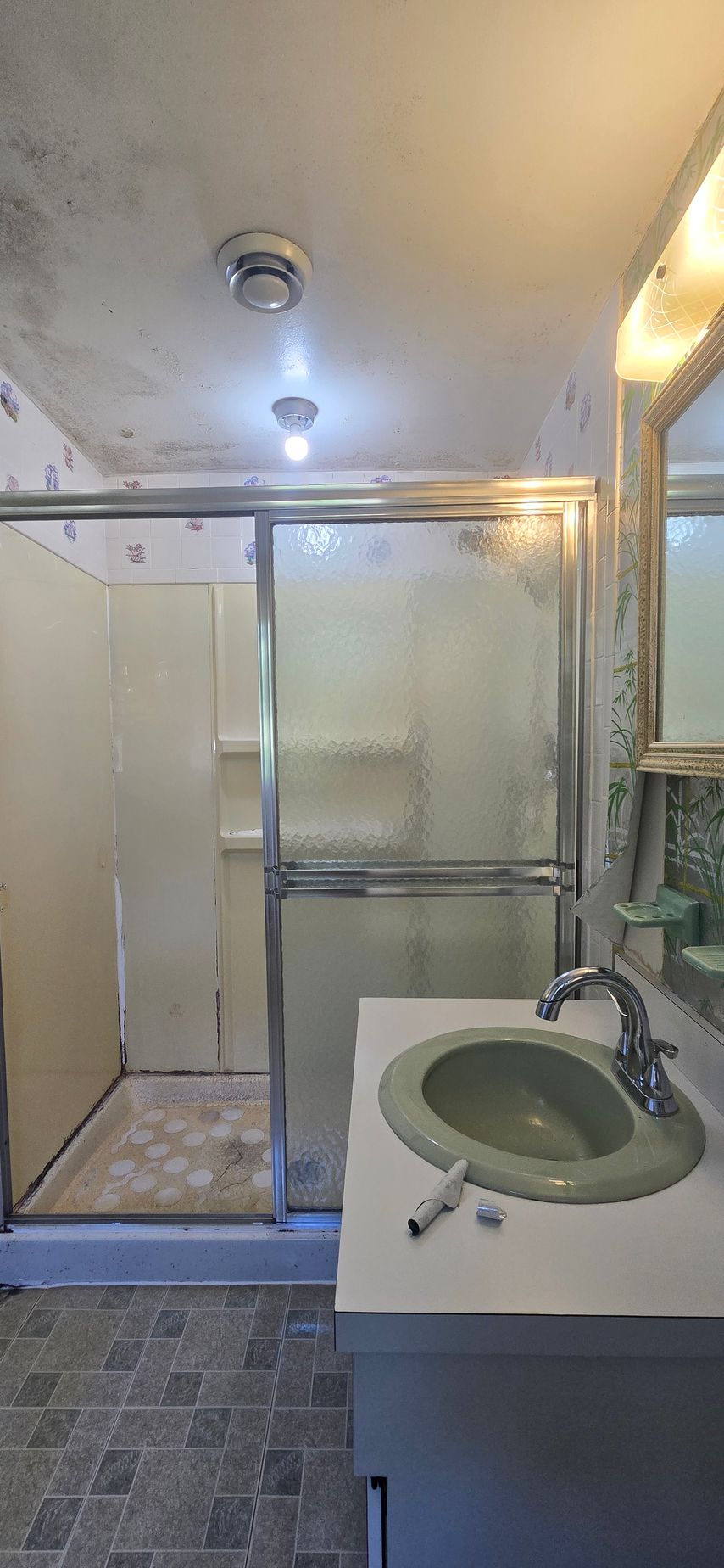 Small bathroom with glass shower stall, beige tile, and a sink vanity in the foreground.