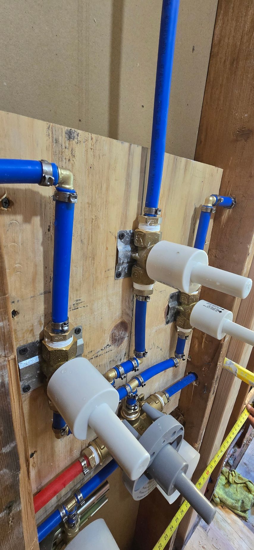 Blue and white plumbing pipes and valves mounted on a plywood wall in a utility area.  By First Choice Bathroom Remodeling done in East Hartford, CT.