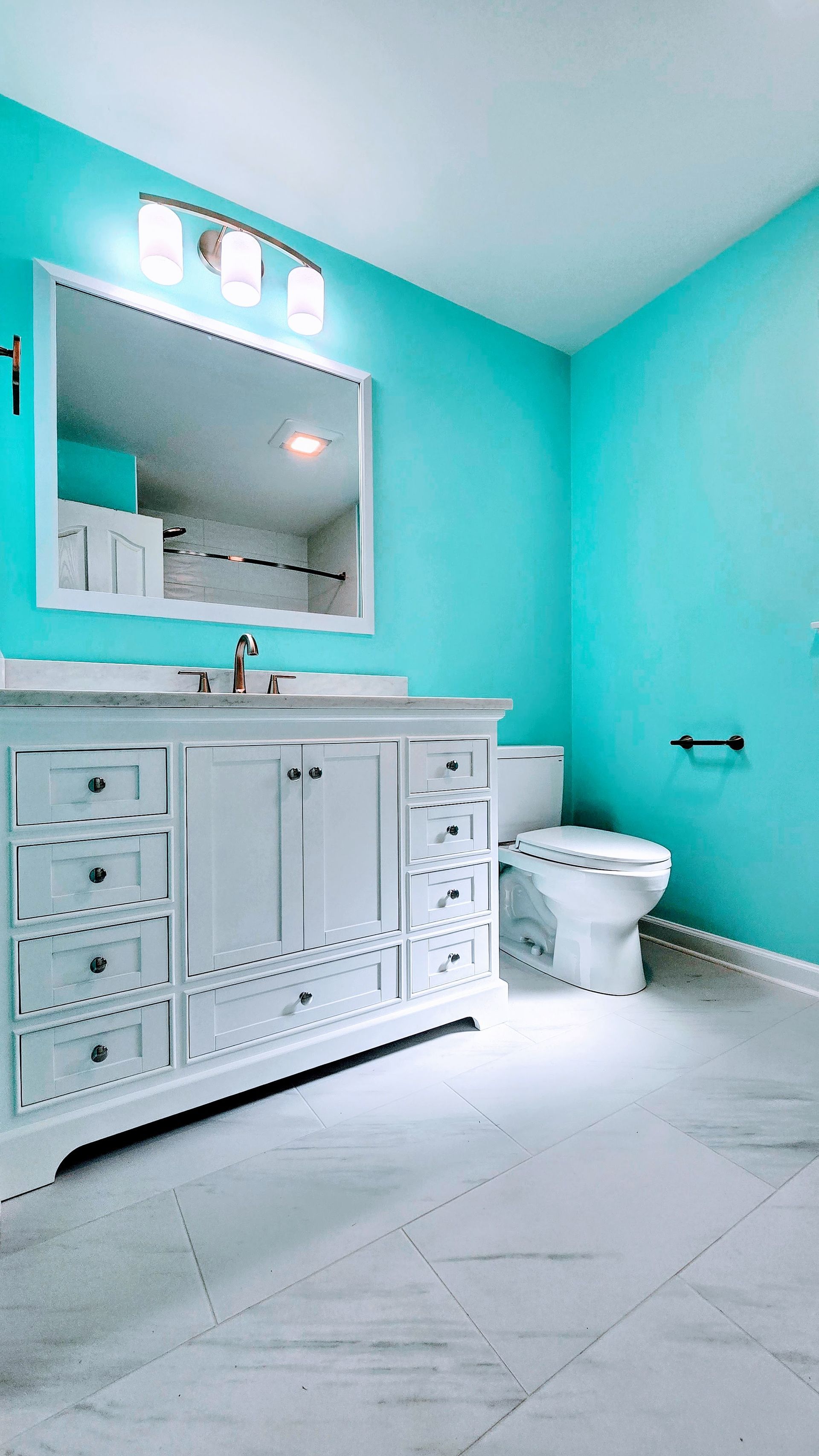 Bright turquoise bathroom with white vanity, mirror, toilet, and light marble floor. By First Choice Bathroom Remodeling done in Southbury, CT.
