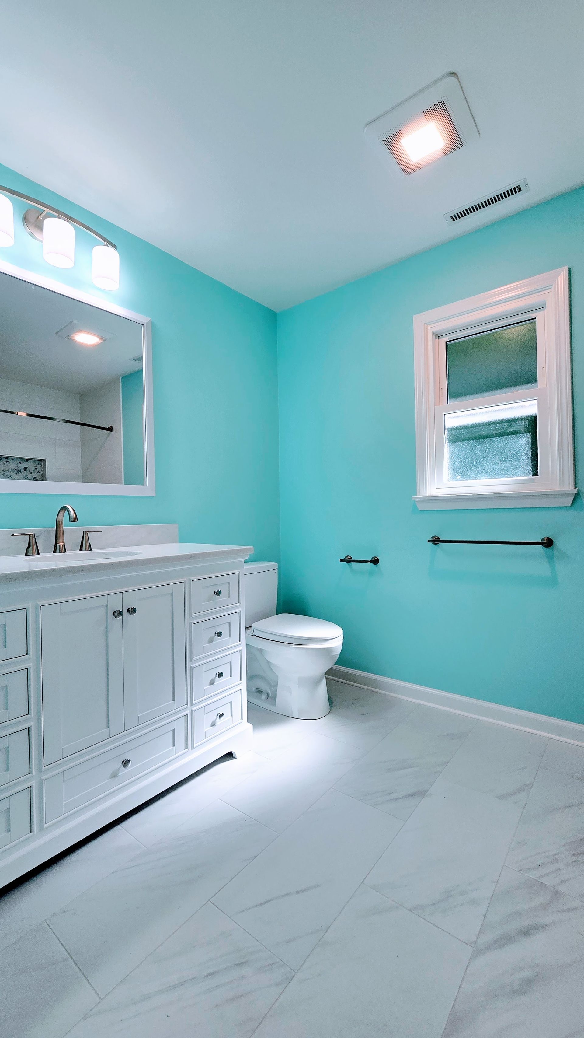 Bright turquoise bathroom with white marble floor, vanity, toilet, window, and shower curtain. Southbury CT