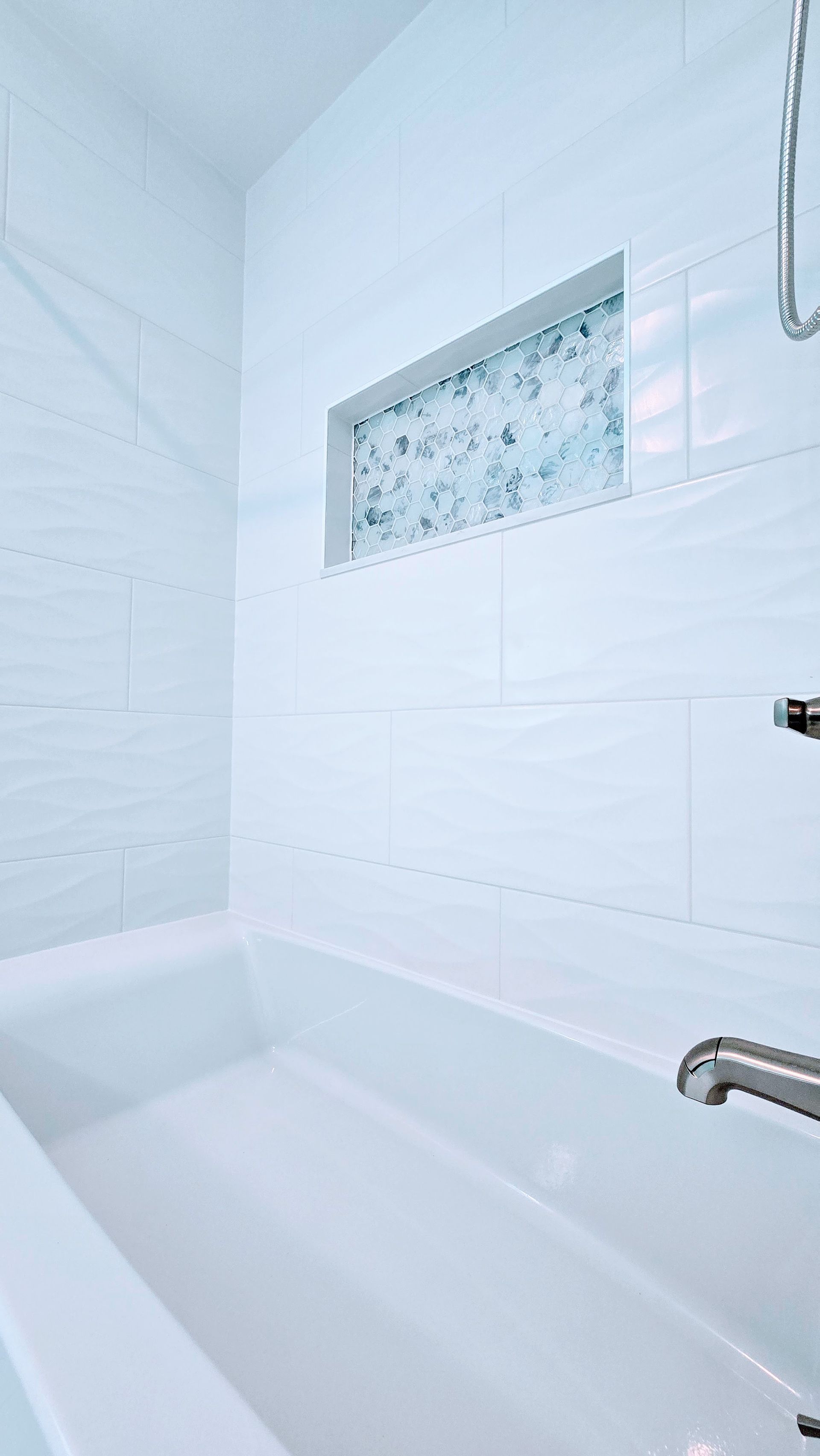 White tiled bathroom with a bathtub, chrome showerhead, and a small frosted glass window. By First Choice Bathroom Remodeling done in Southbury, CT.