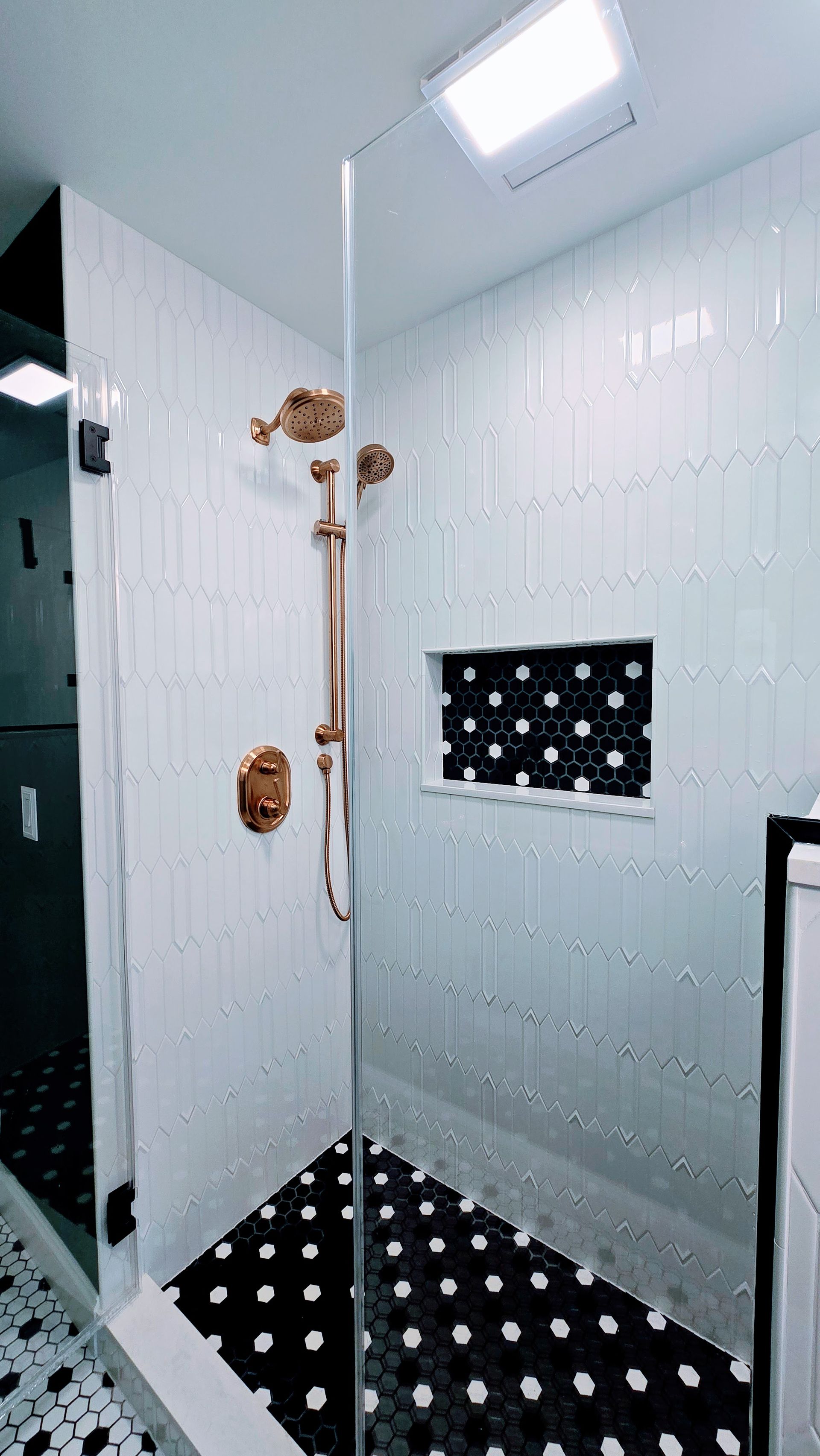 Modern shower with white tile walls, black-and-white floor, glass door, and a square shelf niche. Manchester, CT