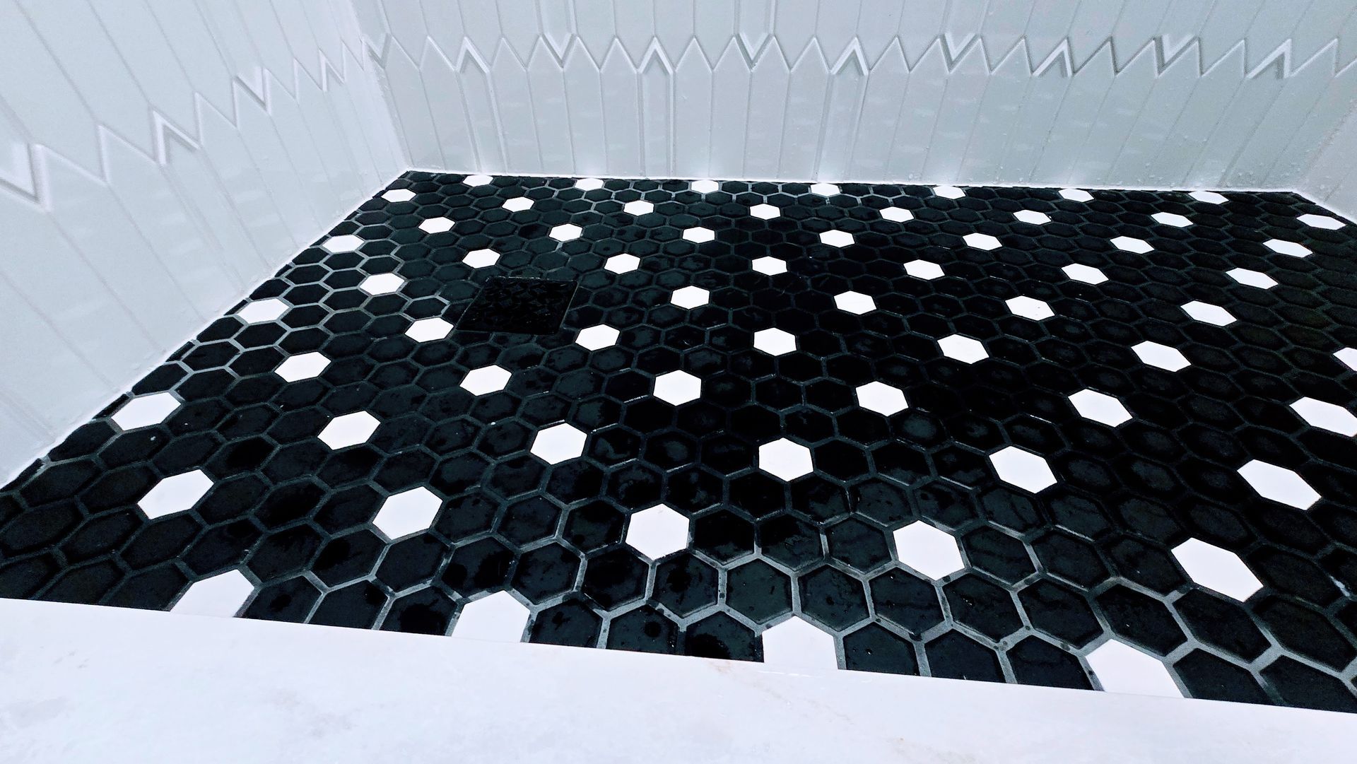 Black hexagonal tile floor with white flower-like accents in a small tiled room. Manchester CT