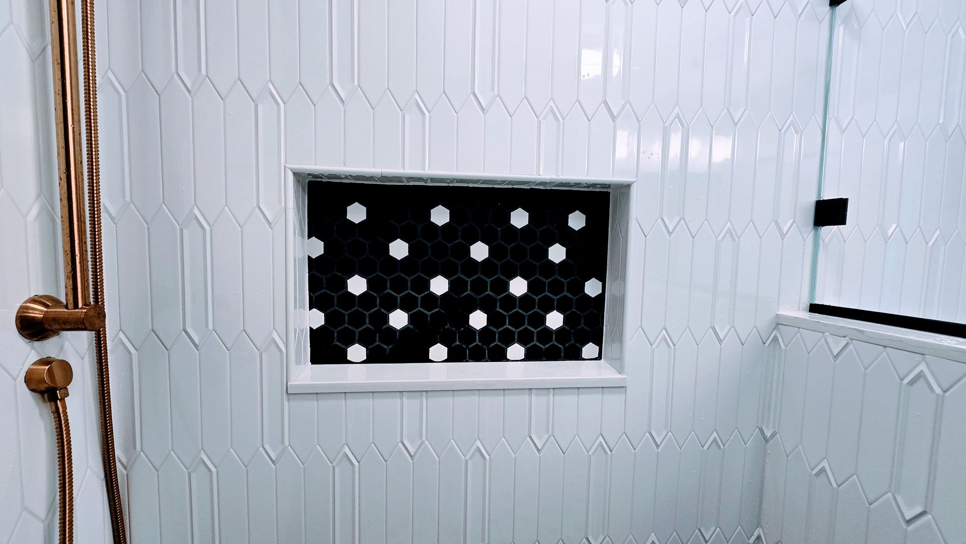White tiled wall with a black recessed panel dotted with white circles and a wooden door handle at left. Manchester CT