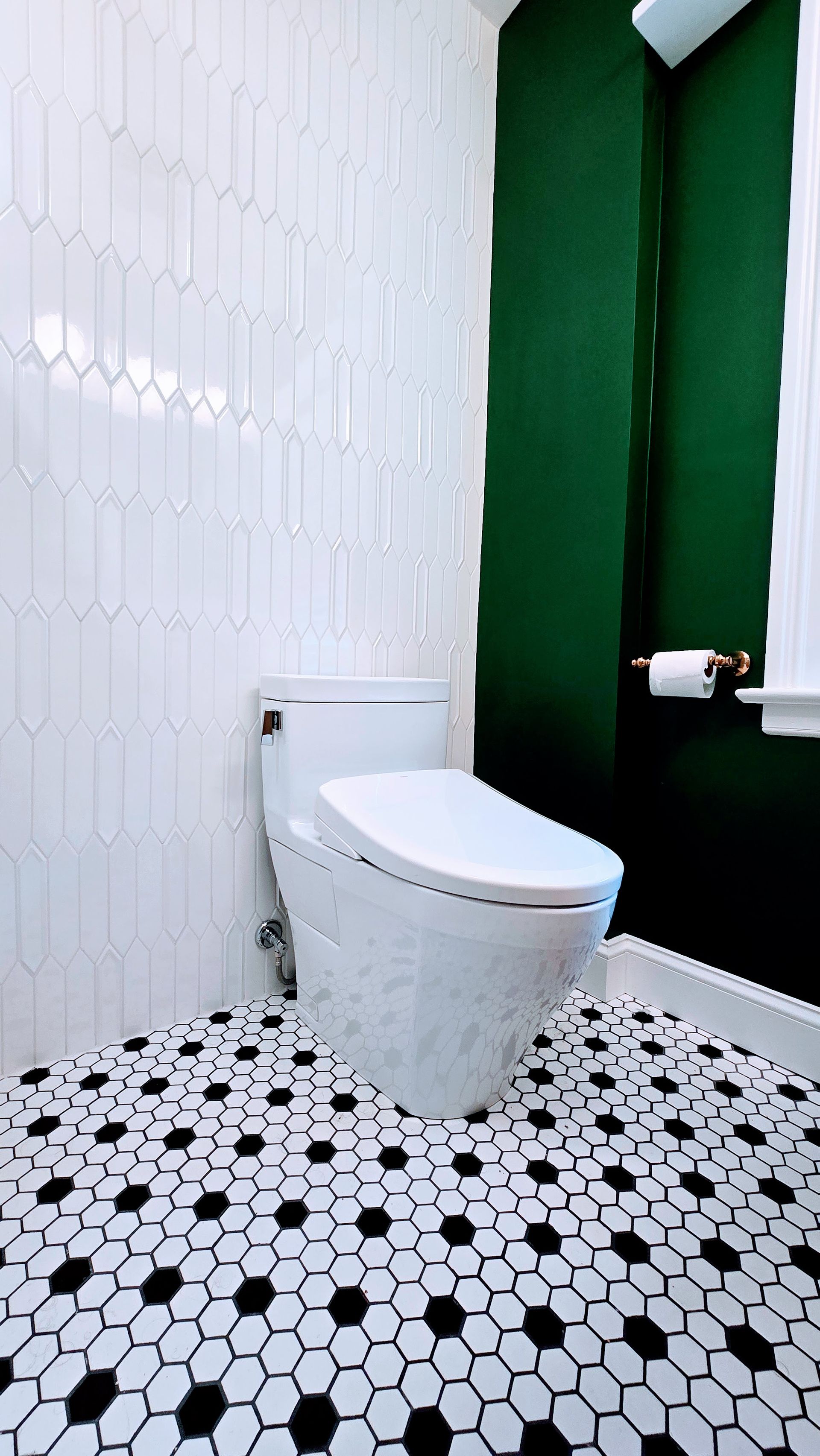 Modern bathroom with white toilet, black-and-white hex tile floor, white wall tiles, and dark green accent walls. Done by First Choice Bathroom Remodeling done in Manchester, CT.