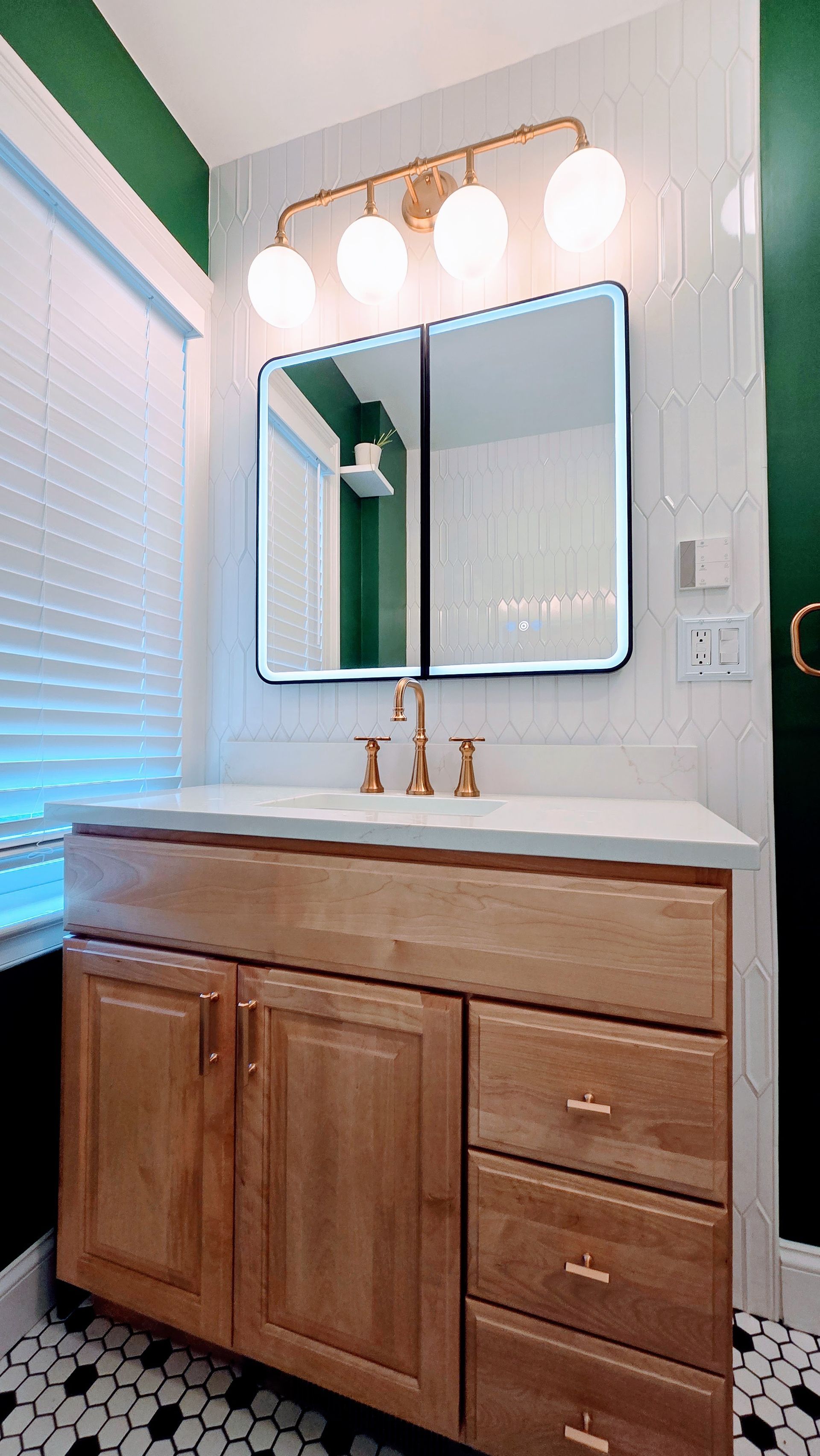 Bathroom vanity with wood cabinet, white countertop, round mirror, and three globe lights. Manchester, CT