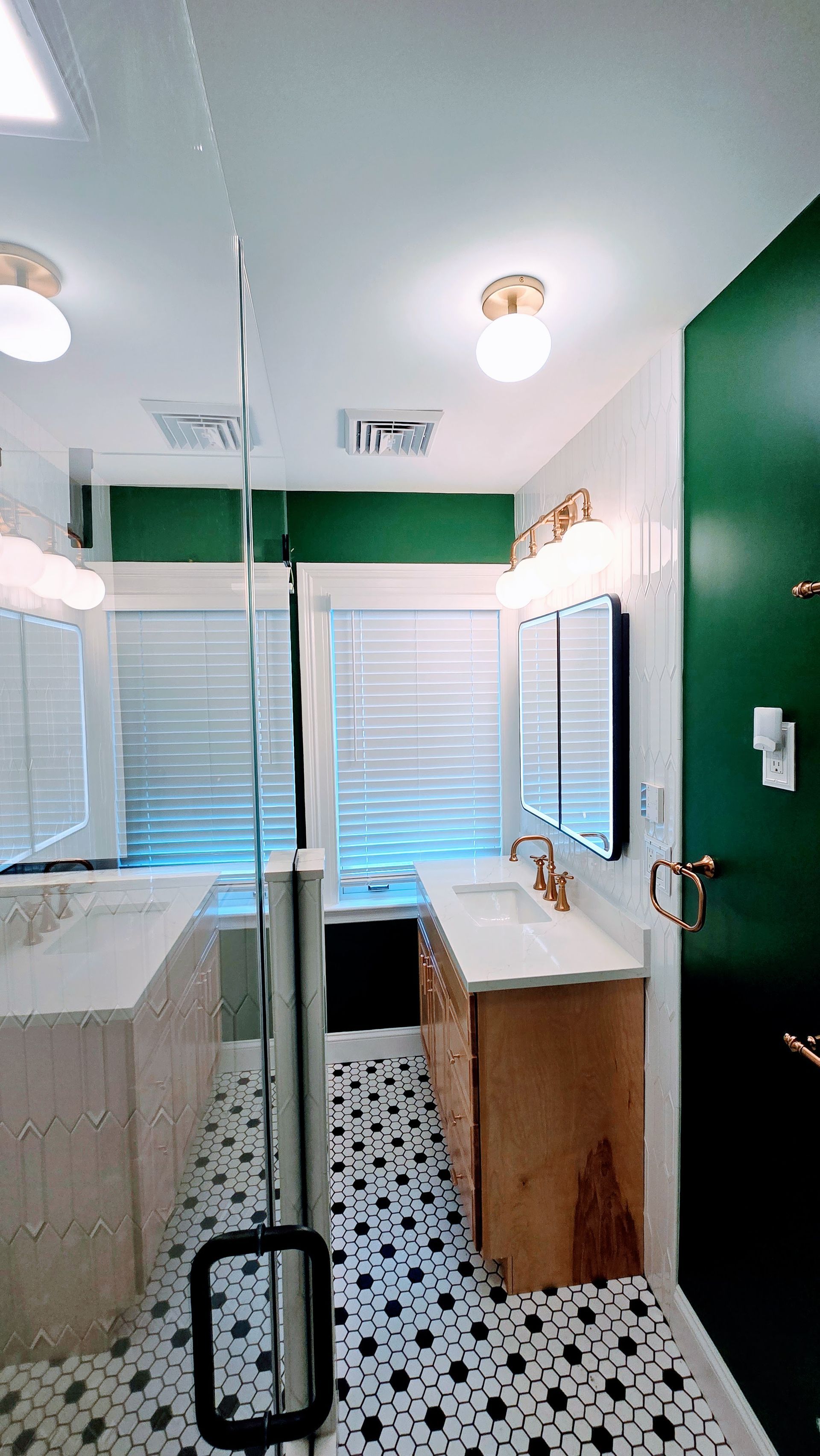 Modern bathroom with green walls, patterned tile floor, vanity, mirror, shower, and a window with blinds. Done by First Choice Bathroom Remodeling done in Manchester, CT.