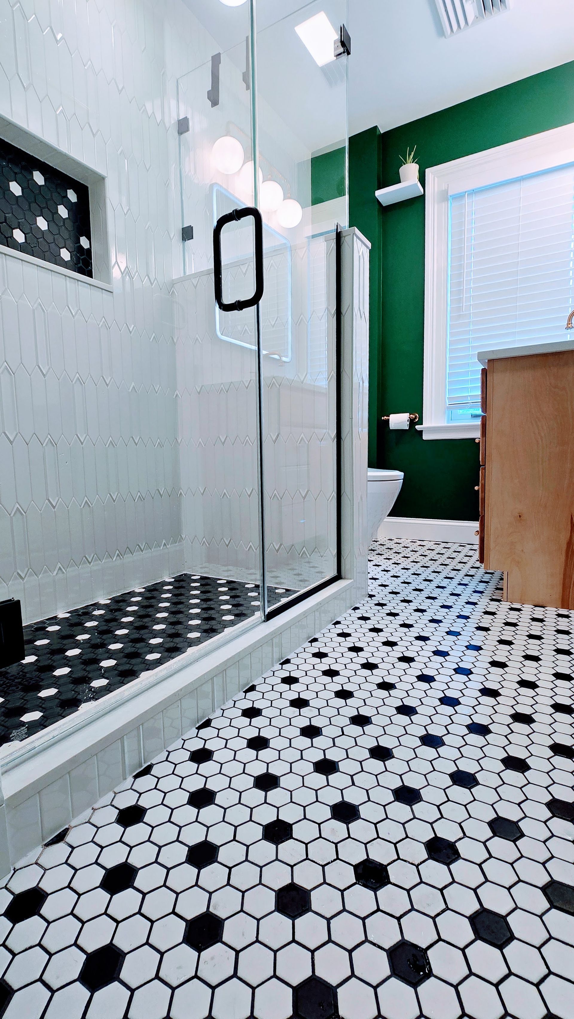 Modern bathroom with black-and-white hex tile, glass shower, and green accent wall. Manchester, CT