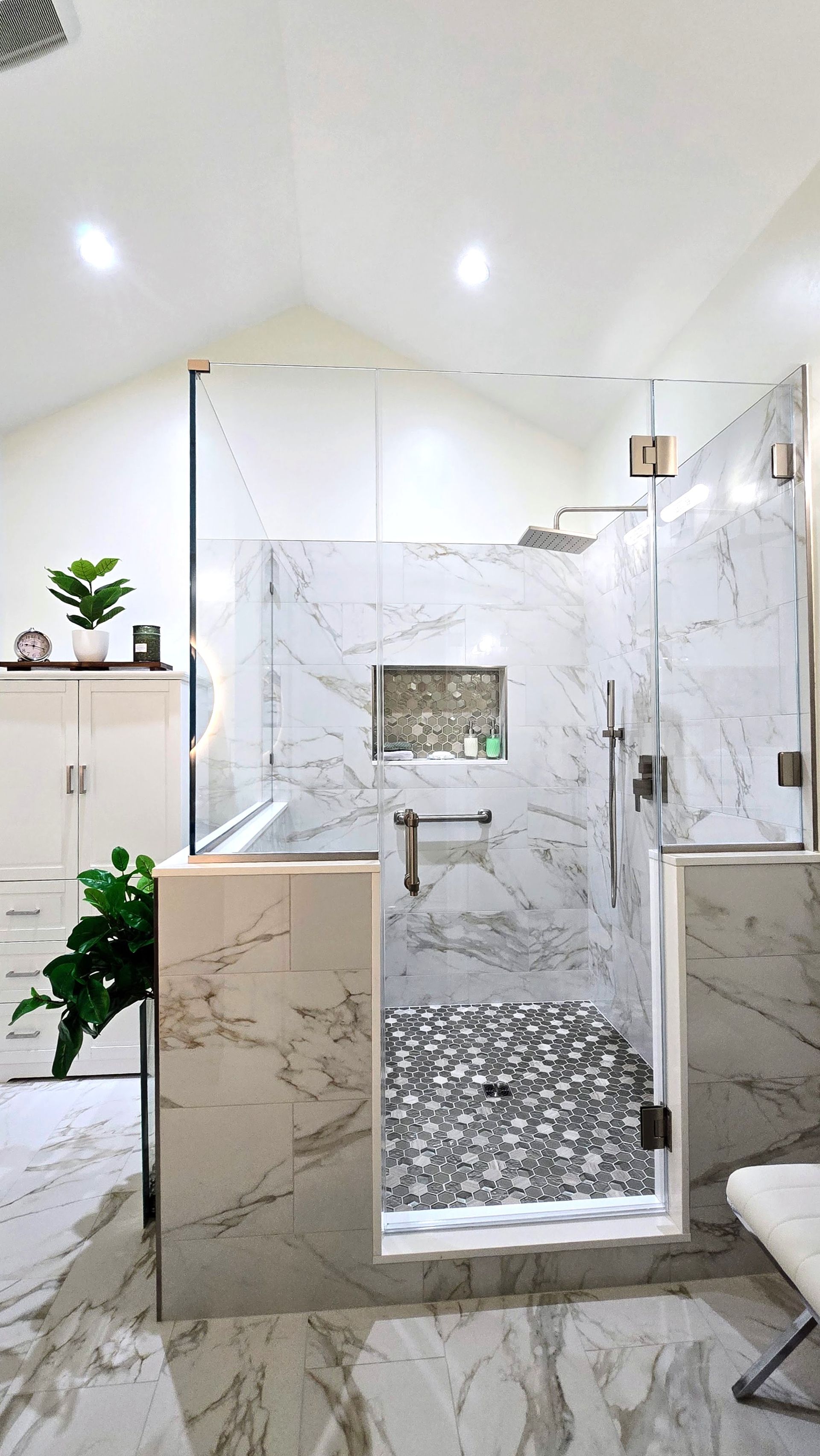 Modern marble-tiled shower with glass door, mosaic floor, and white bathroom walls. By First Choice Bathroom Remodeling done in Prospect, CT.
