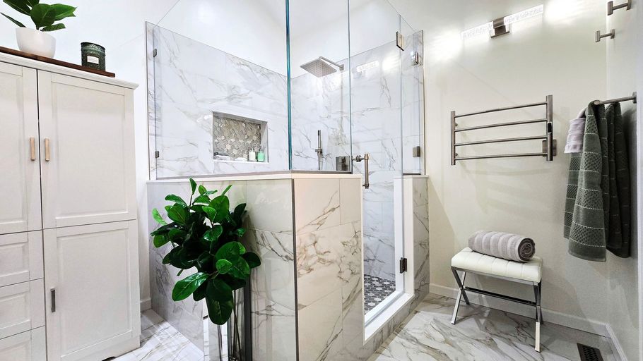 Bright white bathroom remodel in Prospect, CT with glass shower, marble vanity, towel rack, and potted plant