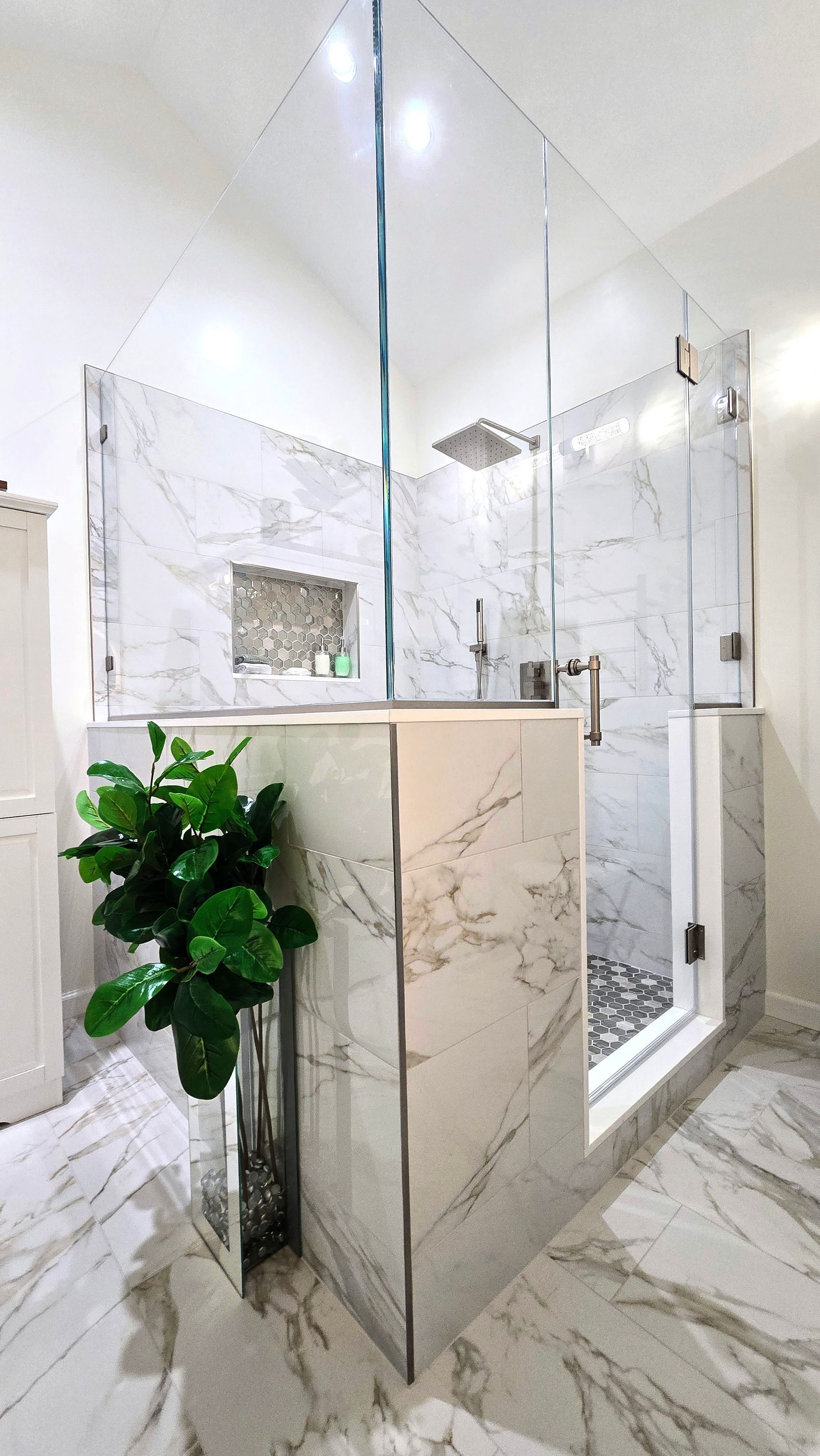 Modern bathroom with marble-look tile, glass shower, vanity mirror, and a potted plant. By First Choice Bathroom Remodeling done in Prospect, CT.