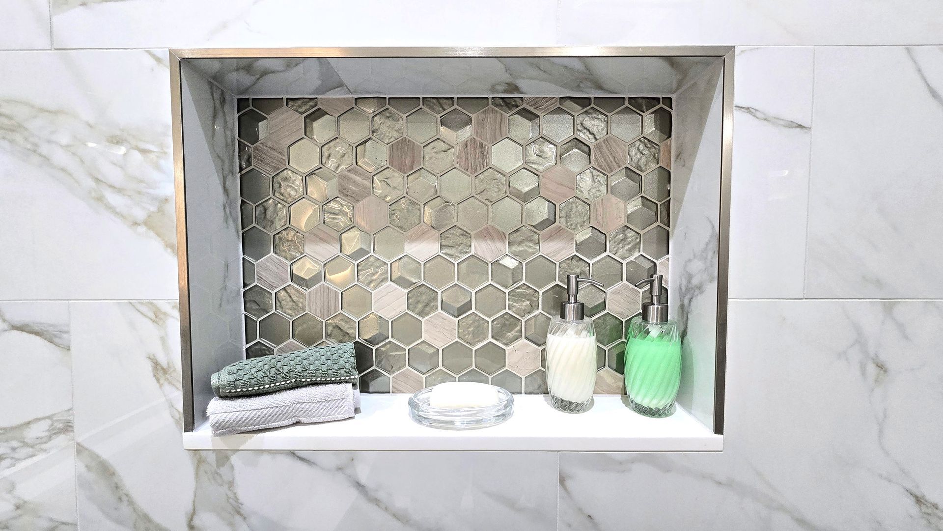 Hex-tile shower niche with bath items: soap, bottle, cup, and sponge on a marble wall. By First Choice Bathroom Remodeling done in Prospect, CT.