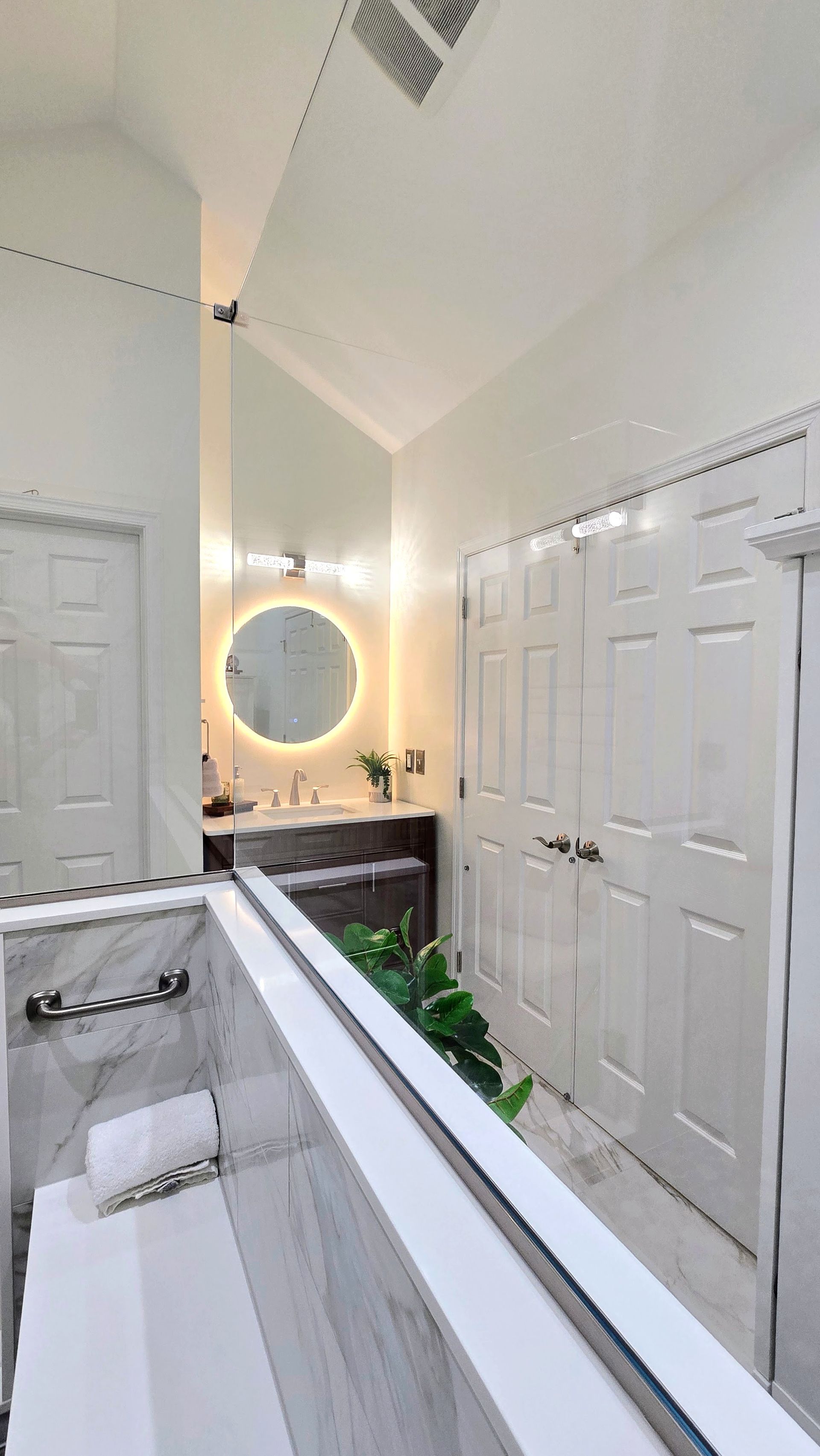 Bright bathroom with double vanity, round mirror, and white closet doors under vaulted ceiling. By First Choice Bathroom Remodeling done in Prospect, CT.