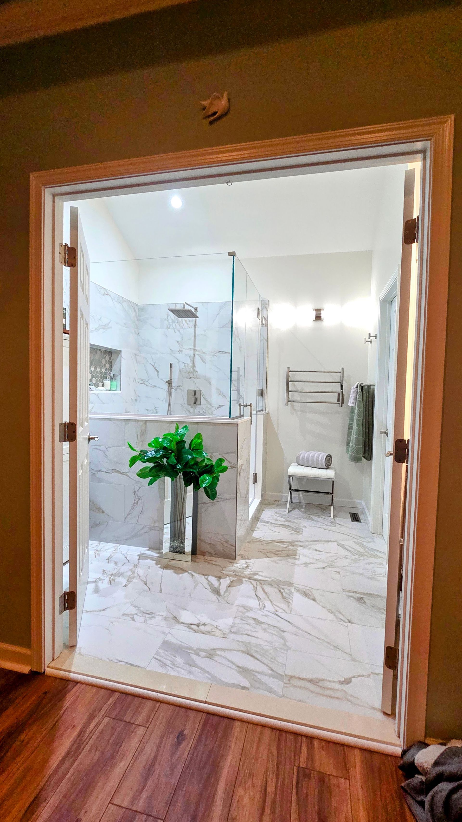 Open bathroom doorway in Prospect, CT with white marble tile, glass shower, and a vase of green flowers.