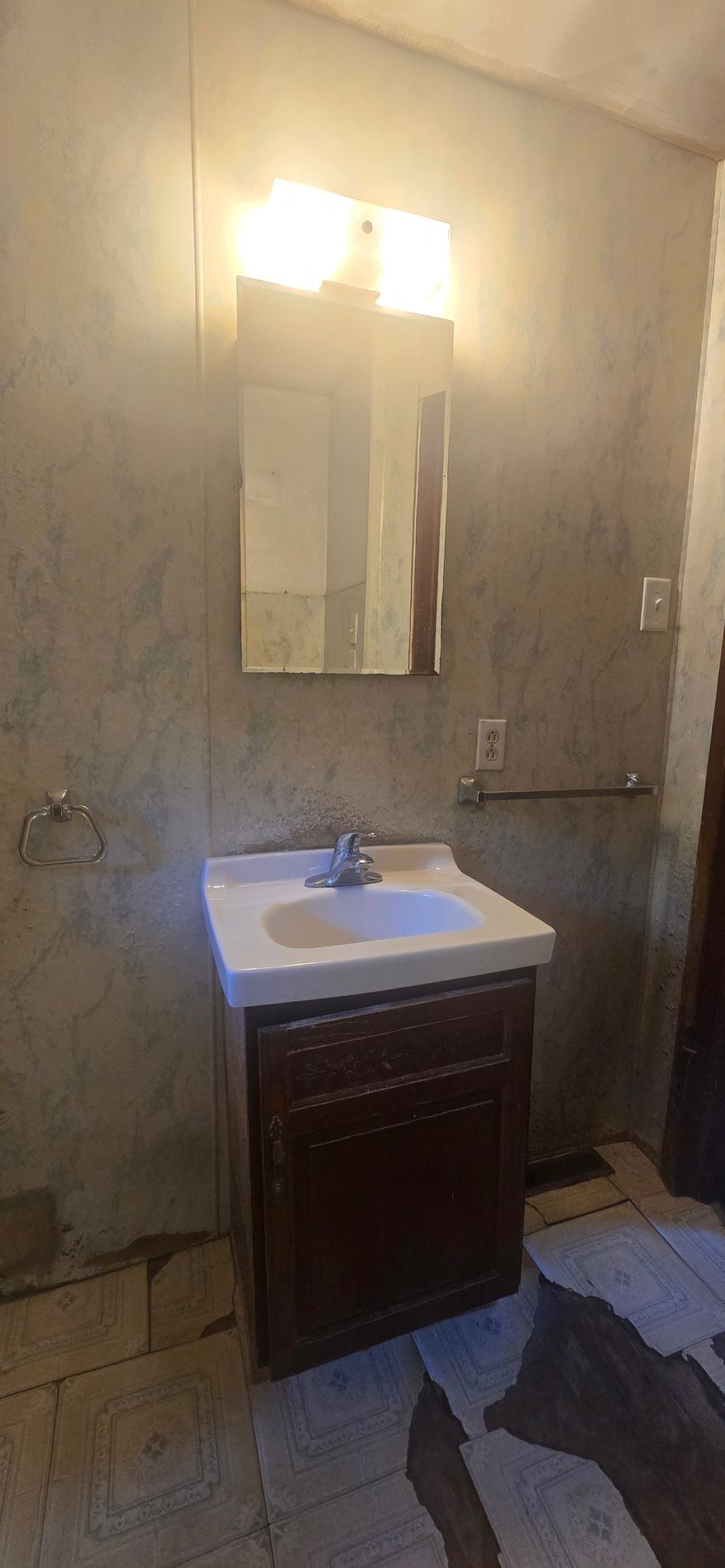 Small bathroom with a vanity sink, mirror, wall lights, and unfinished concrete walls.