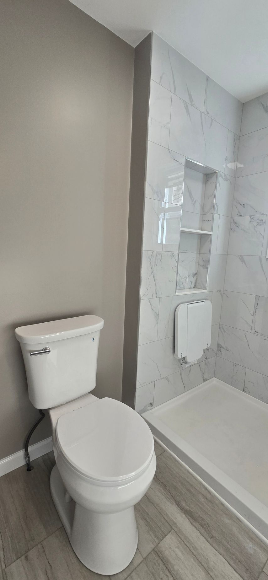Small bathroom with a white toilet beside a glass shower and white tile walls. By First Choice Bathroom Remodeling done in Cheshire, CT.