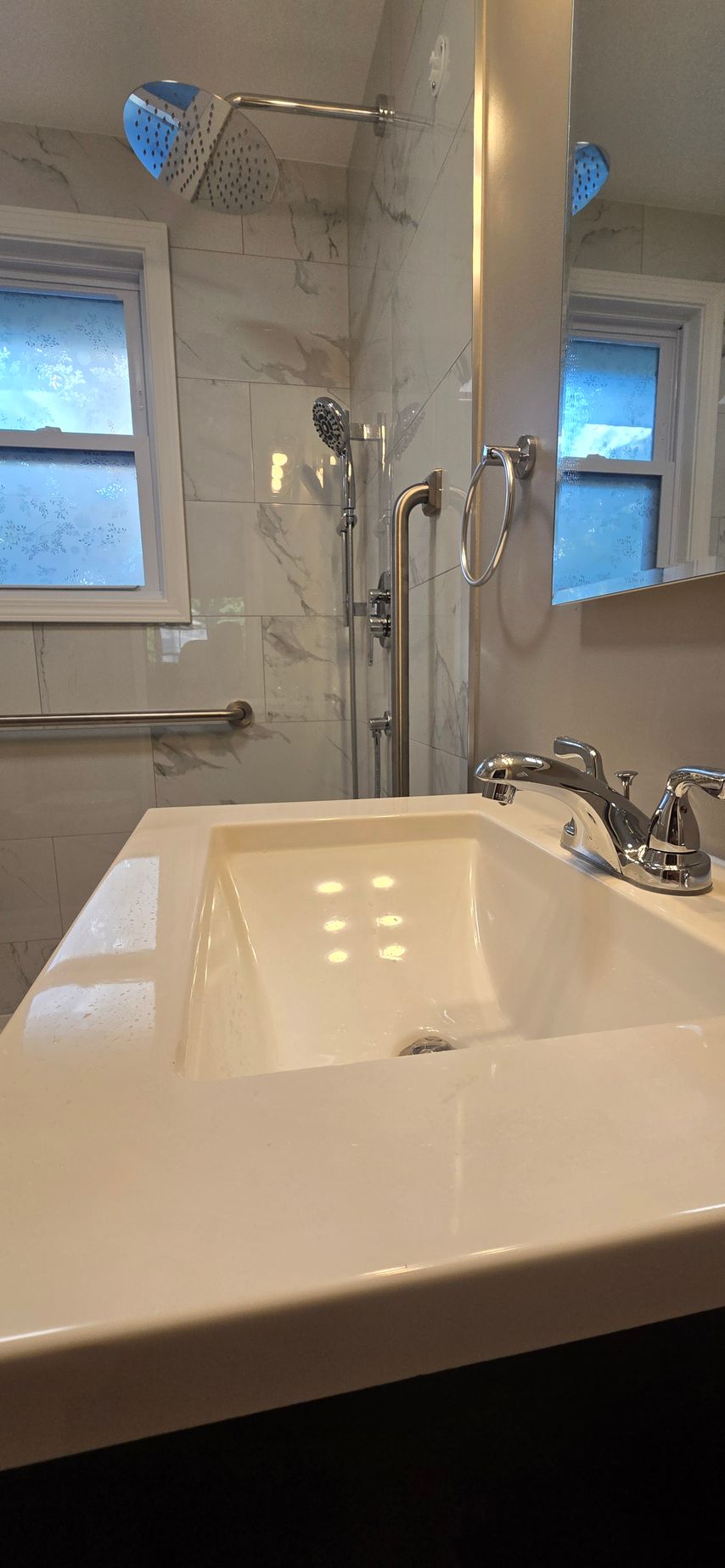 Bathroom with white sink, chrome faucet, mirror, and tiled shower area with two windows. By First Choice Bathroom Remodeling done in Cheshire, CT.