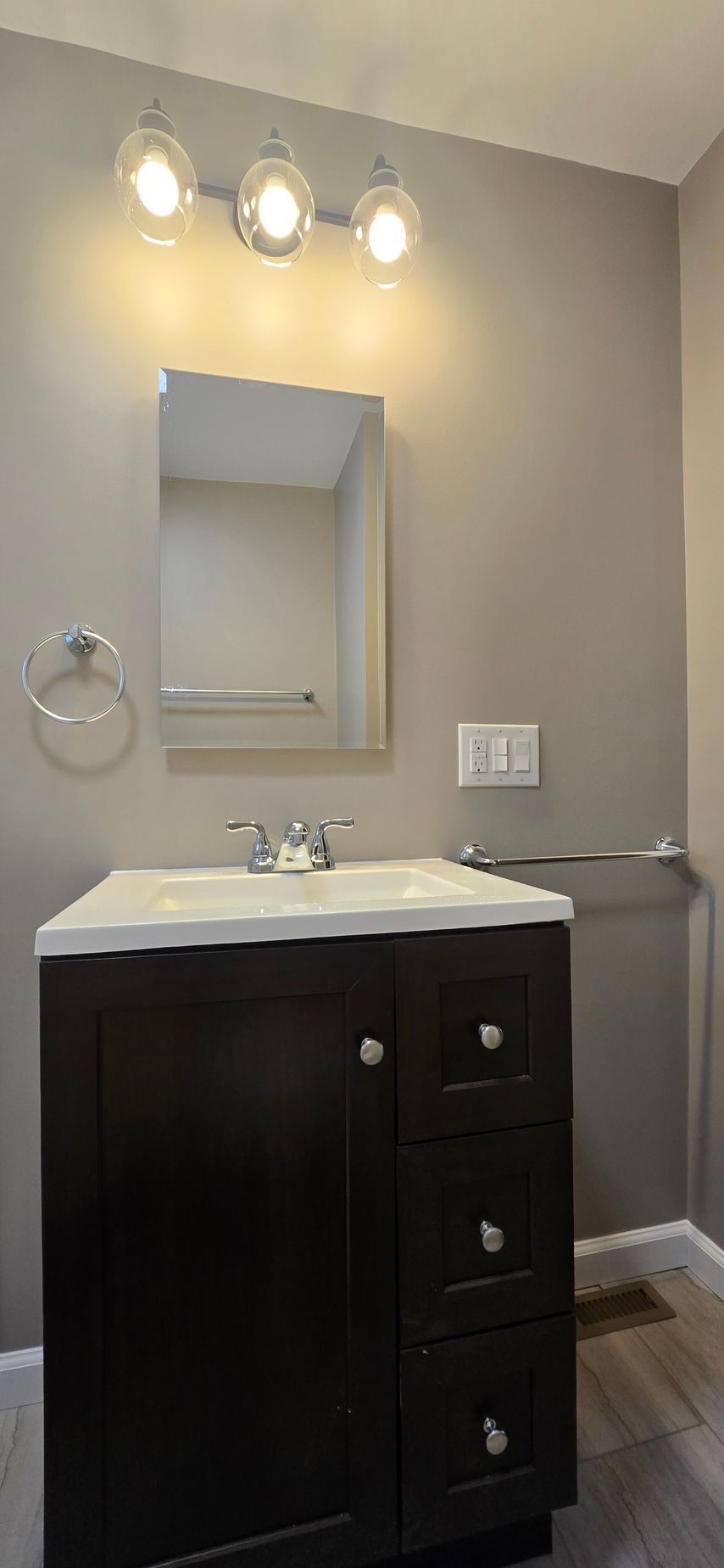 Modern bathroom vanity with black cabinet, white sink, mirror, and three lights above. By First Choice Bathroom Remodeling done in Cheshire, CT.