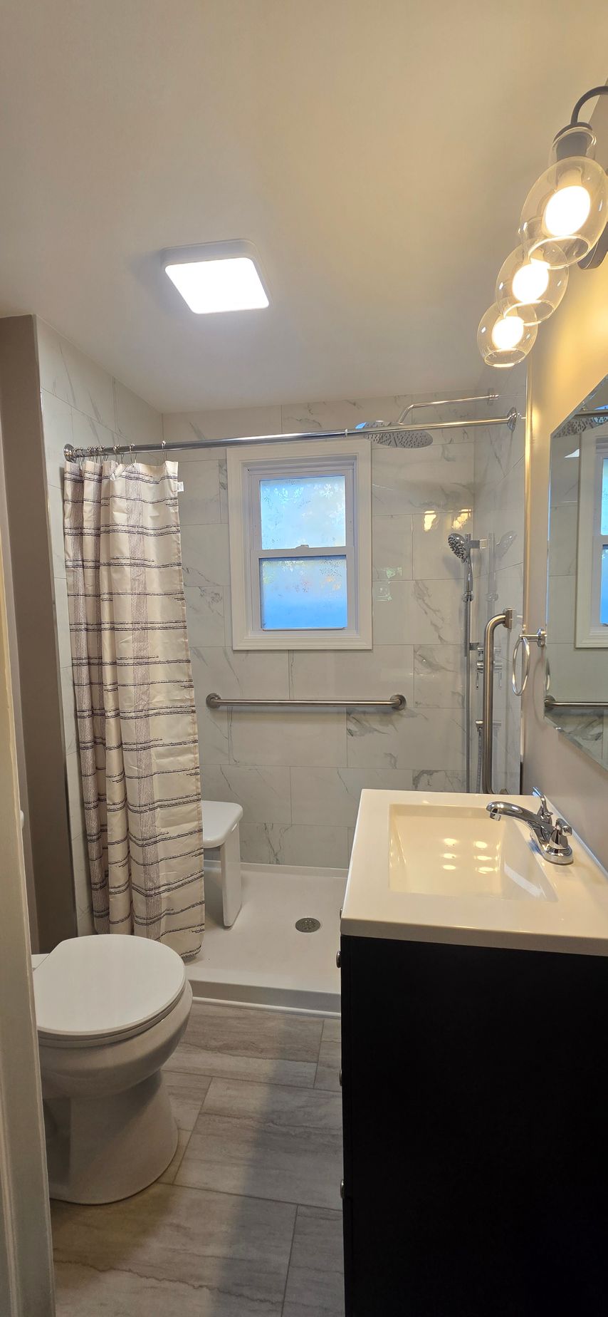 Small bathroom with toilet, walk-in shower, vanity sink, window, and overhead lights. By First Choice Bathroom Remodeling done in Cheshire, CT.